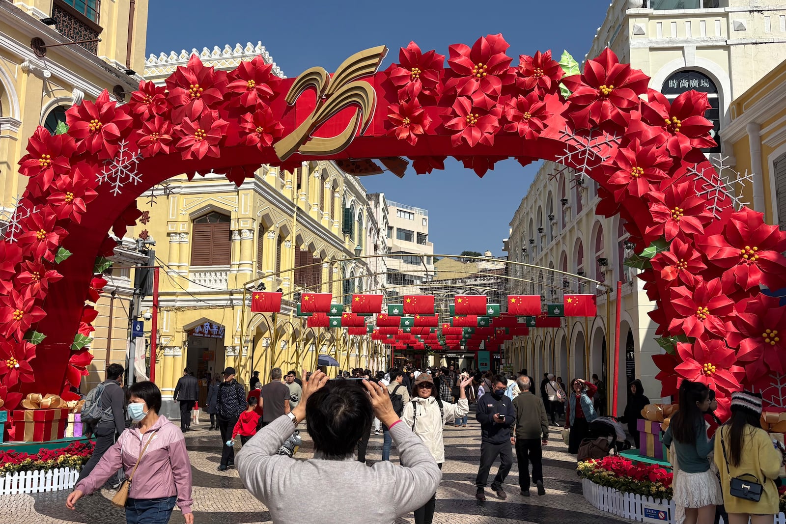 Tourists take photos in front of an installation that marks the 25th anniversary of Macao's handover to Chinese rule in Macao on Dec. 13, 2024. (AP Photo/Kanis Leung)