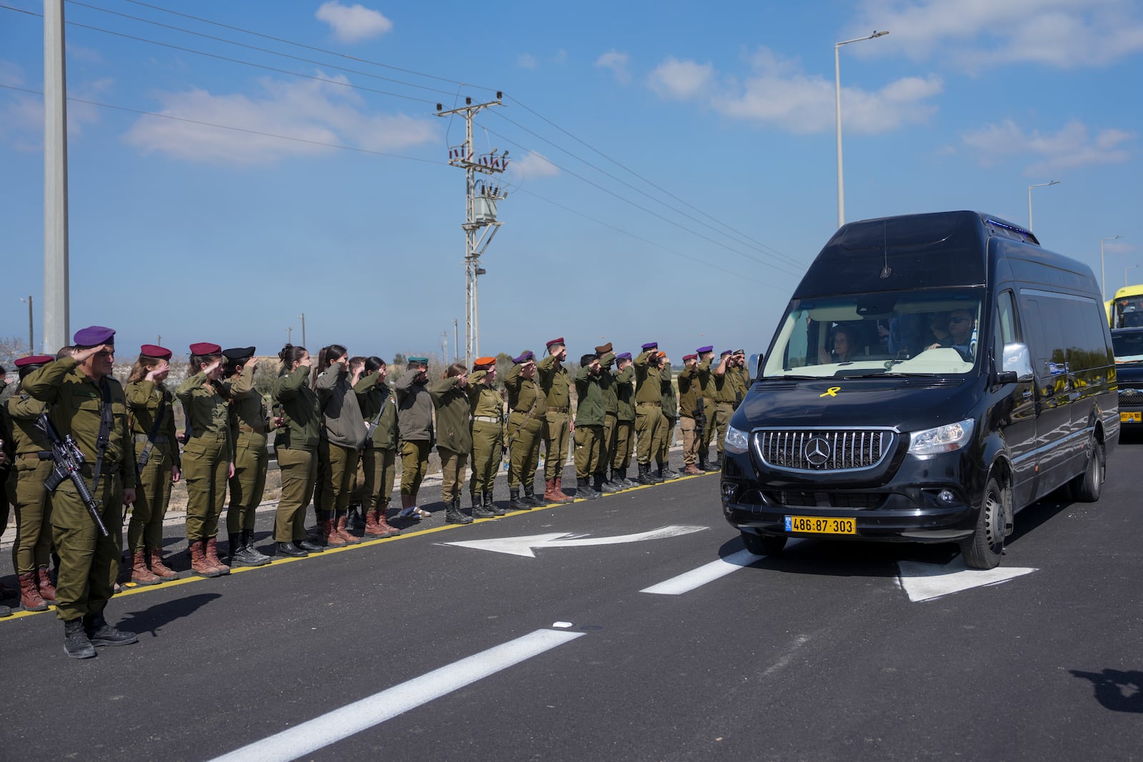 Israeli soldiers salute as the convoy carrying the coffins of slain hostages Shiri Bibas and her two children, Ariel and Kfir, pass by near Kibbutz Nir Oz, southern Israel, Wednesday, Feb. 26, 2025. The mother and her two children were abducted by Hamas on Oct. 7, 2023, and their remains were returned from Gaza to Israel last week as part of a ceasefire agreement with Hamas. (AP Photo/Ohad Zwigenberg)