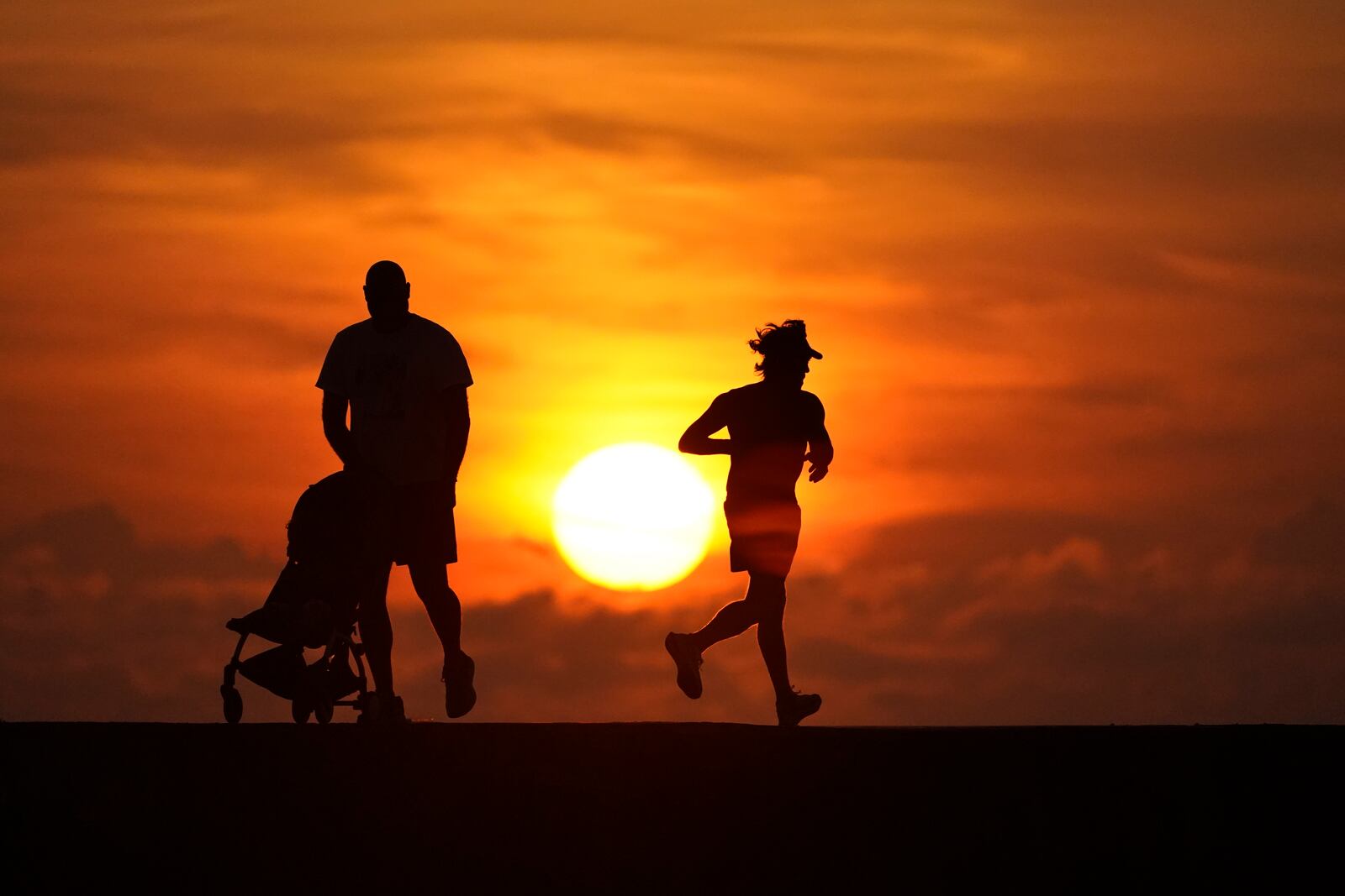 FILE - Walkers and joggers are silhouetted on a jetty as the sun rises over the Atlantic Ocean, Saturday, Sept. 19, 2020, in Bal Harbour, Fla. (AP Photo/Wilfredo Lee, File)