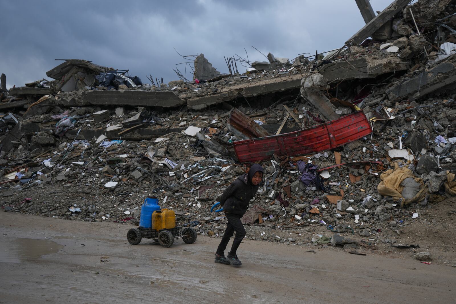 A young Palestinian kid carries water along the destruction caused by the Israeli air and ground offensive in Jabaliya, Gaza Strip, Thursday, Feb. 6, 2025. (AP Photo/Abdel Kareem Hana)