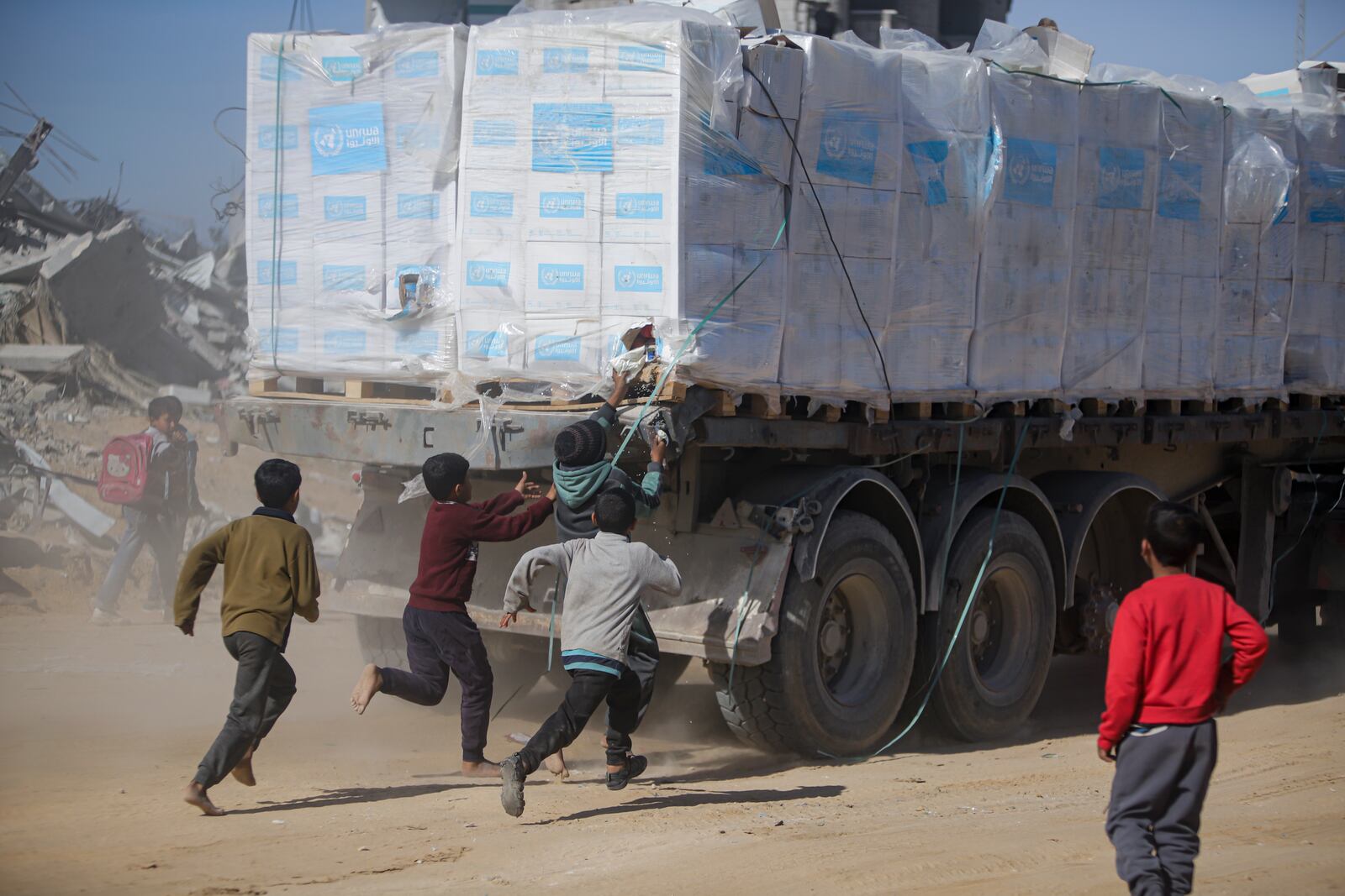 Palestinians chase humanitarian aid trucks that arrived through the Kerem Shalom crossing from Egypt into the Gaza Strip, in Rafah, Tuesday, Jan. 21, 2025. (AP Photo/Jehad Alshrafi)