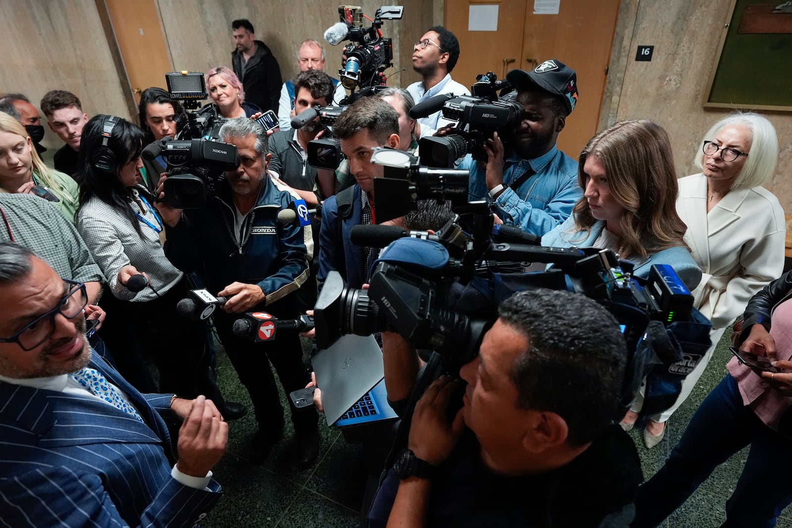 Mahnaz Tayarani, right, in white coat, mother of Nima Momeni, who is charged with murder in Cash App founder Bob Lee's stabbing death, watches as defense attorney Saam Zangeneh, bottom left, speaks to reporters after exiting the courtroom at the Hall of Justice for Momeni's murder trial Tuesday, Dec. 3, 2024, in San Francisco. (AP Photo/Godofredo A. Vásquez)