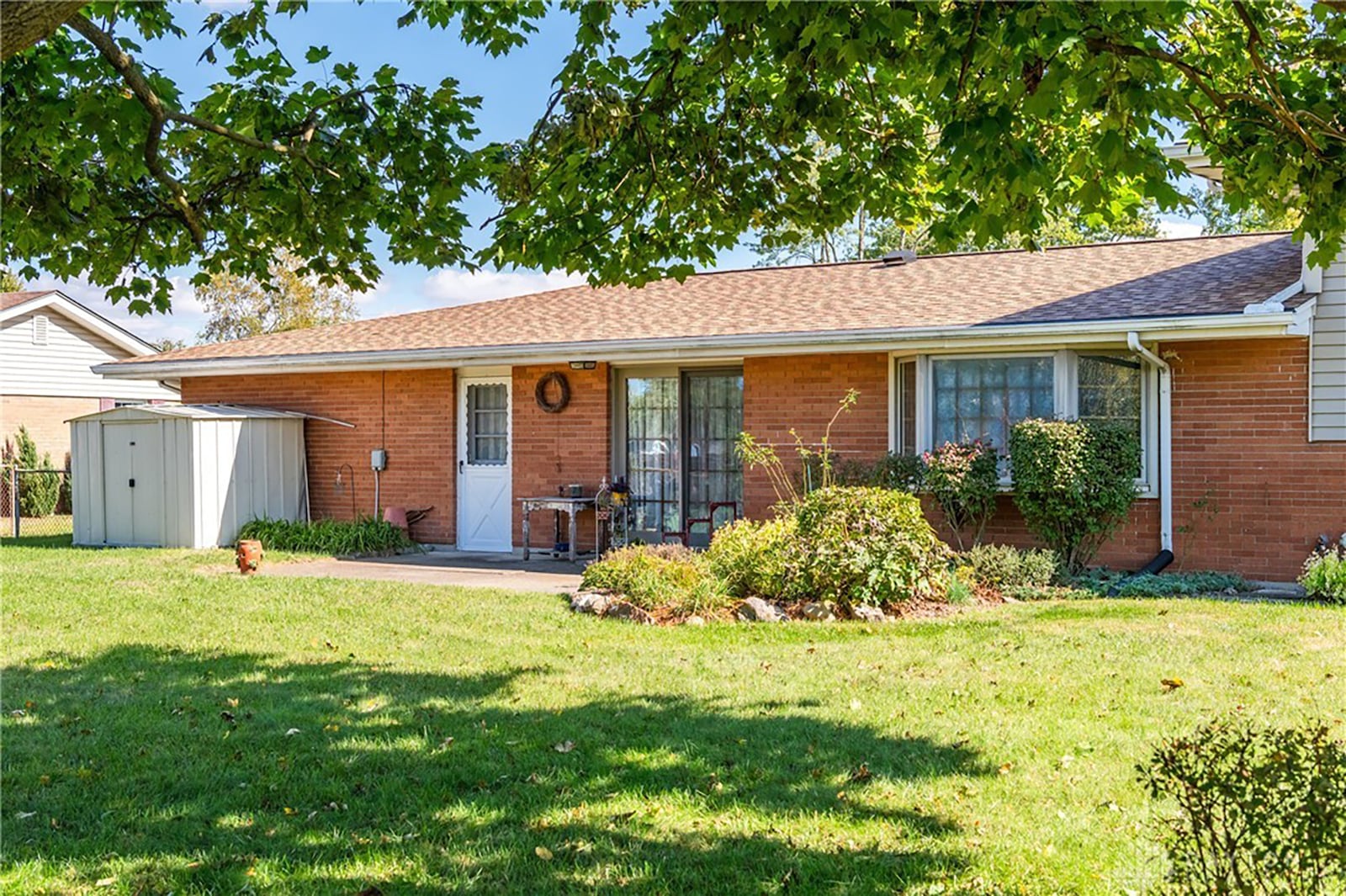 The rear of the brick home has a concrete patio and metal shed.