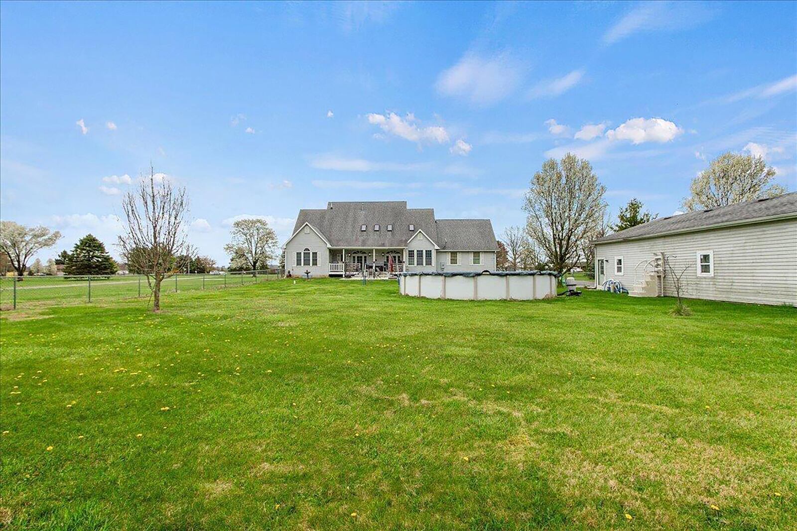 The rear of the home has a covered deck, above-ground pool and two-car detached garage. The lot is partially fenced and has woods at the rear. There are skylights visible on the upper floor.