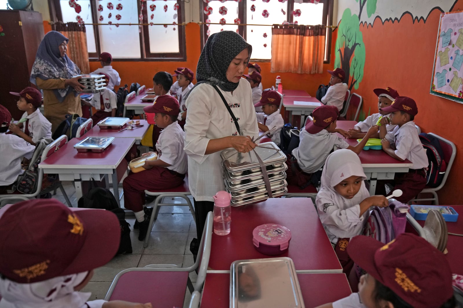 Members of school committee distribute meals to students during the kick off of President Prabowo Subianto's ambitious free meal program to feed children and pregnant women nationwide despite critics saying that its required logistics could hurt Indonesia's state finances and economy, at an elementary school in Depok, West Java, Indonesia, Monday, Jan. 6, 2025. (AP Photo/Dita Alangkara)