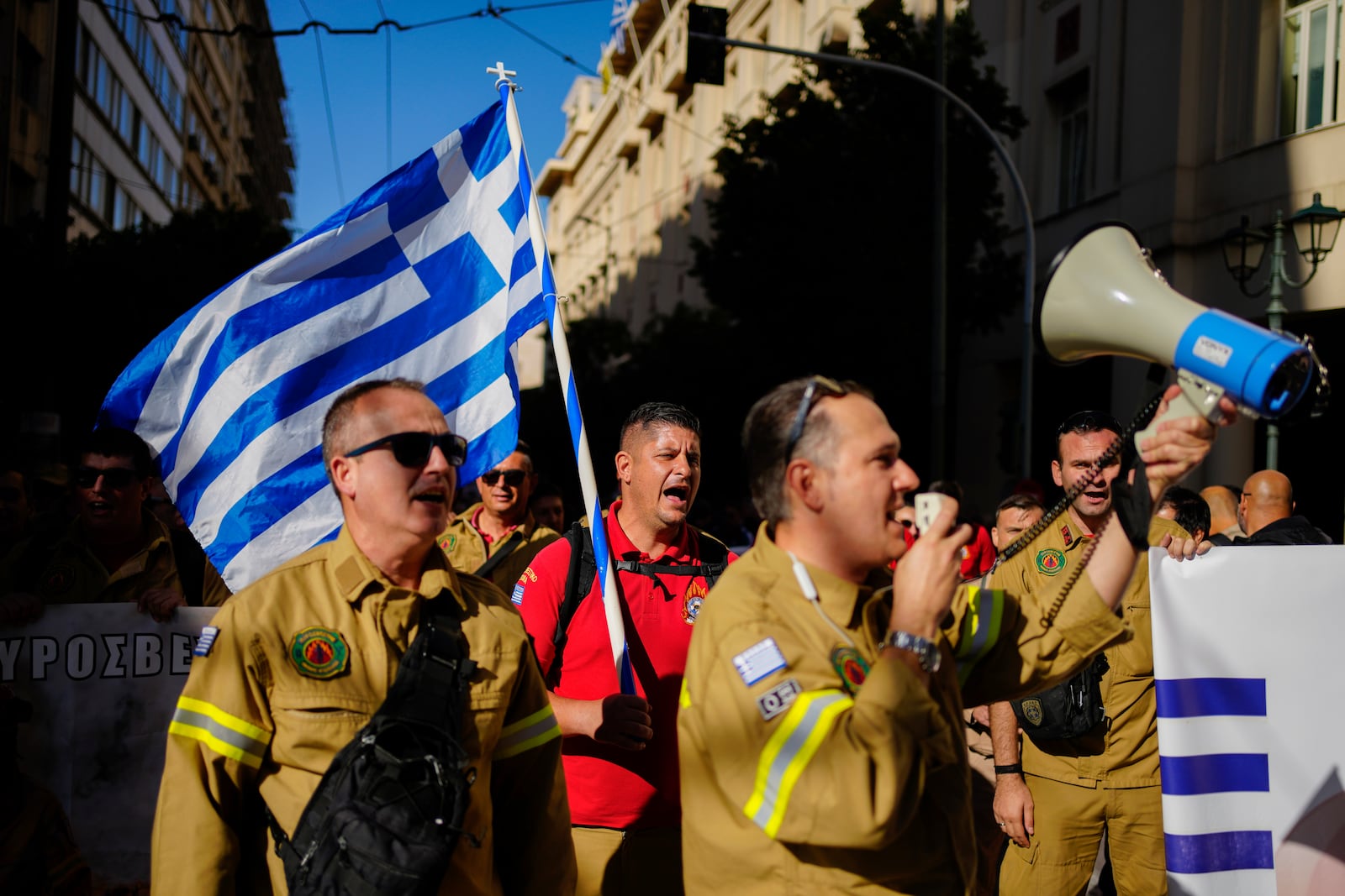 Seasonal firefighters hold a Greek flag as the take part in rally, during a nationwide general strike organized by private and public sector unions demanding for better wages, in Athens, Greece, Wednesday, Nov. 20, 2024. (AP Photo/Thanassis Stavrakis)