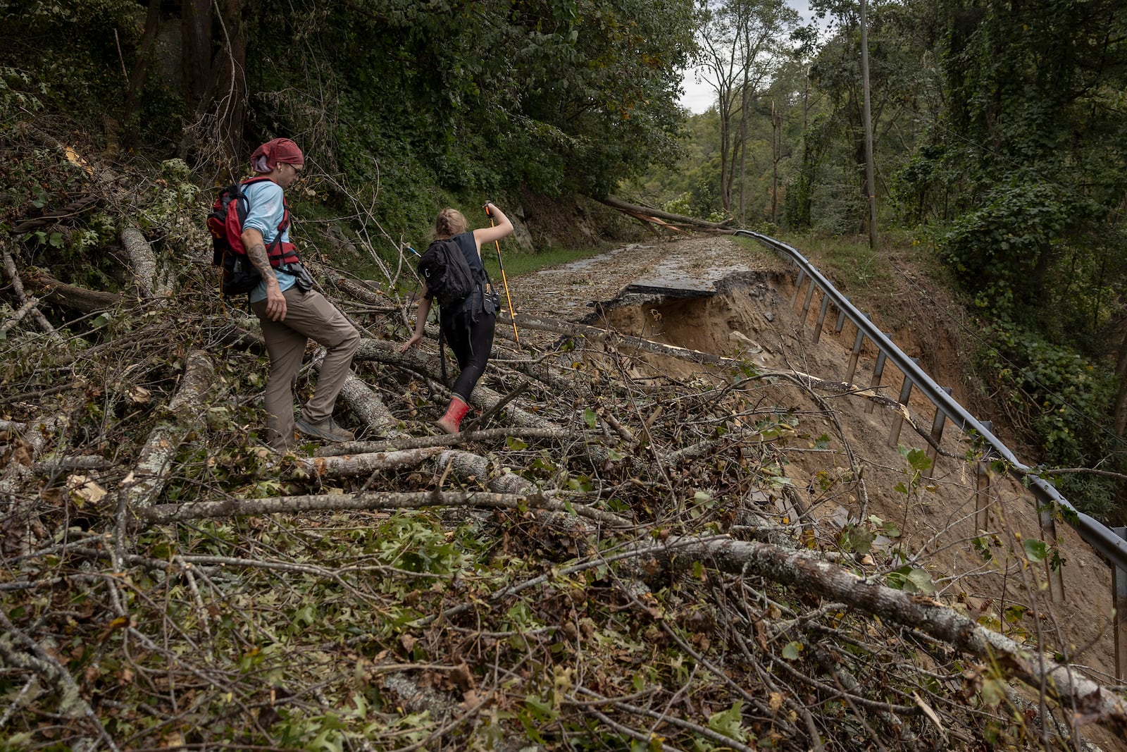 Two people hike along a damaged portion of the Gerton Highway to bring food and supplies to family members stranded in Gerton, N.C., on Tuesday, Oct. 1, 2024. (Christian Monterrosa/The New York Times)
                      