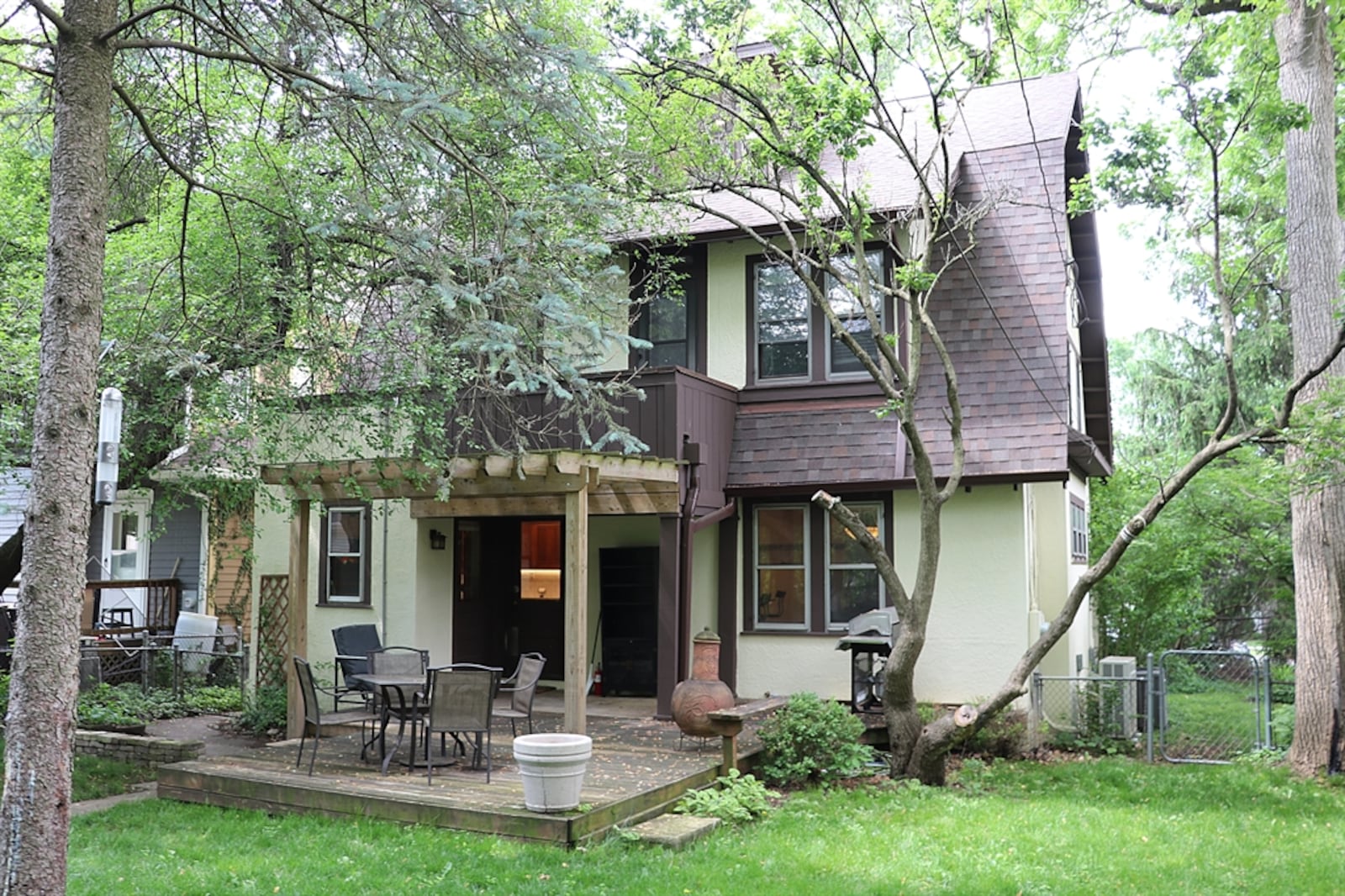 Part of the wooden deck is covered by a pergola; and the backyard is surrounded by a chain-link fence.