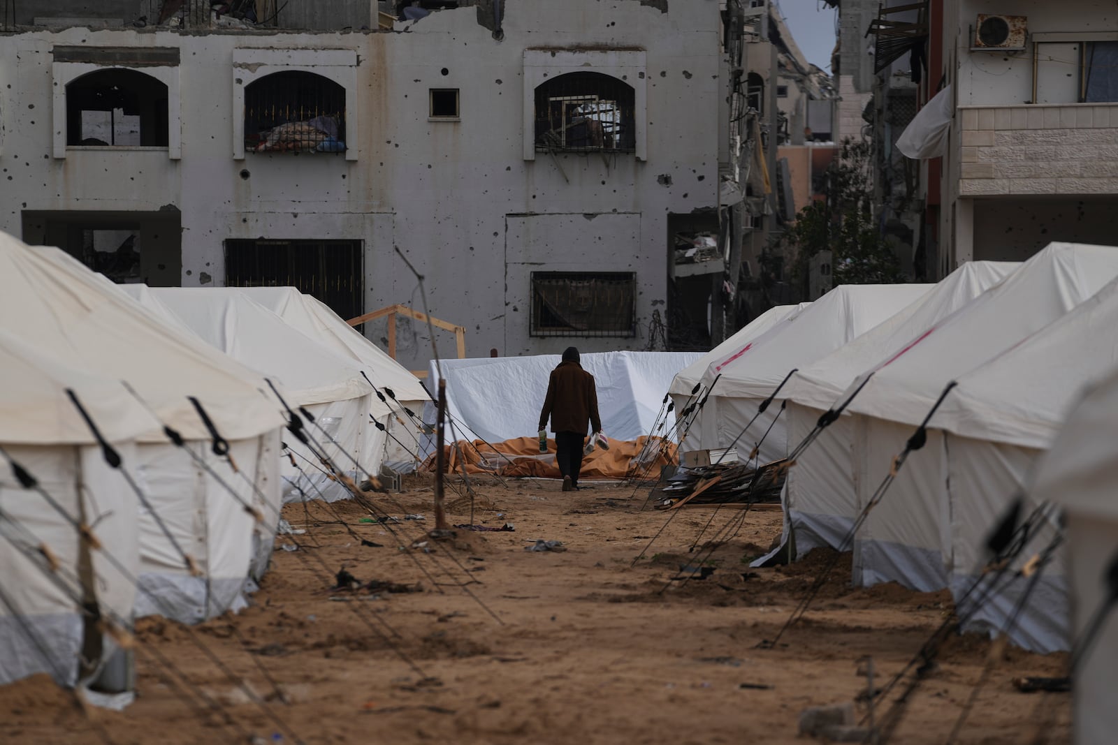 A man walks between tents for displaced Palestinians next to destroyed buildings following the Israeli air and ground offensive in Jabaliya, Gaza Strip, Thursday, Feb. 6, 2025. (AP Photo/Abdel Kareem Hana)