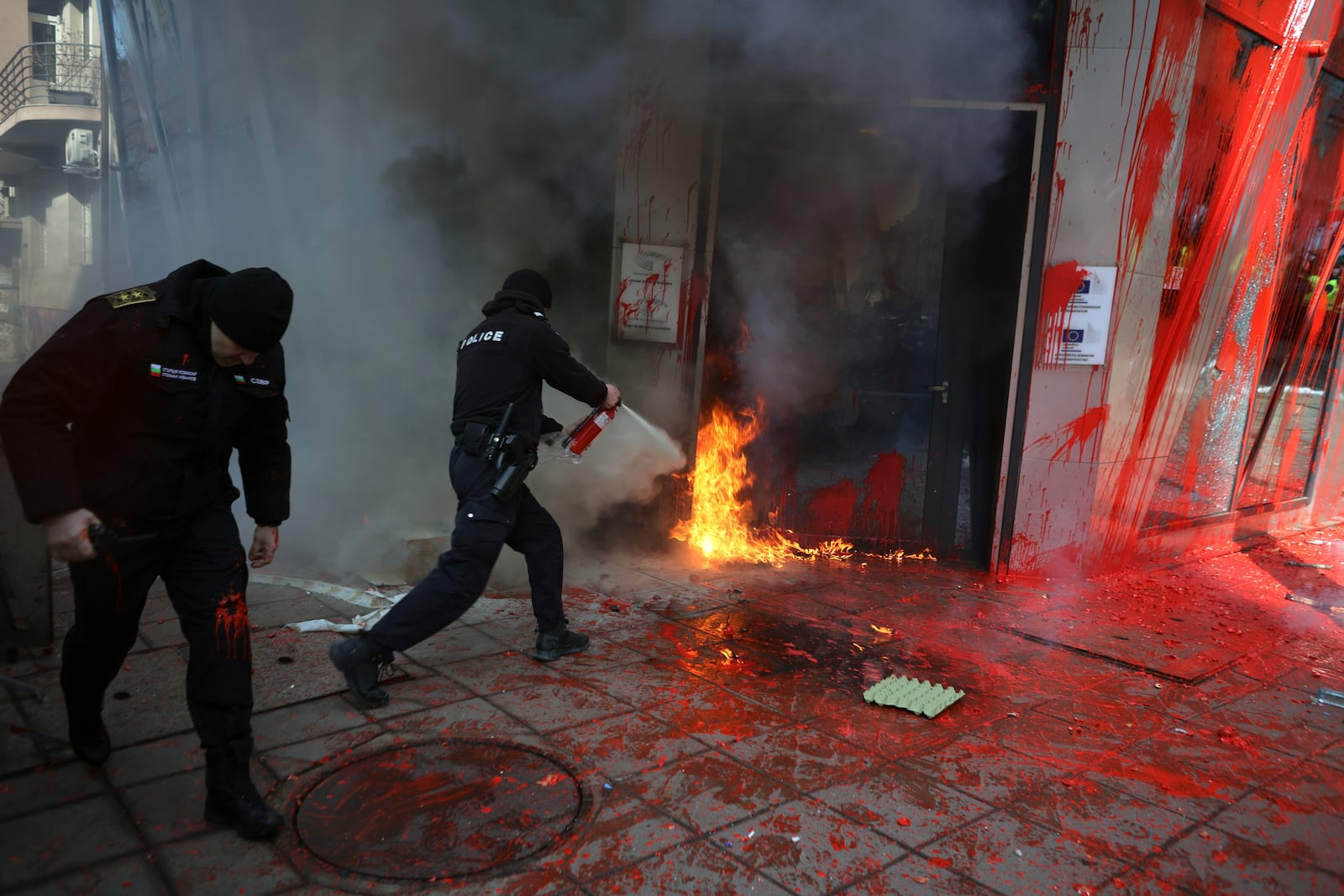 Policeman extinguish a fire set by nationalist protesters at EU commission office door, in Sofia, Saturday, Feb. 22, 2025. (AP Photo/Valentina Petrova)