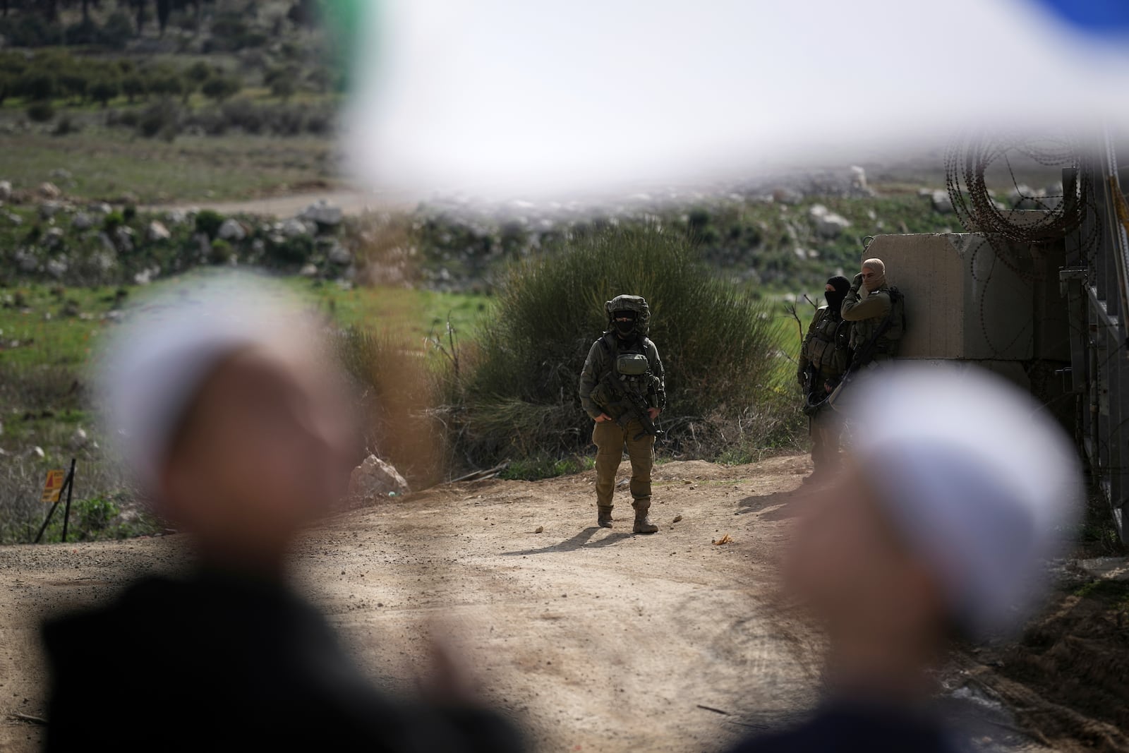 Israeli soldiers stand near members of the Druze community, holding Druze flags, as they wait for buses carrying members of the Syrian Druze community to cross from Syria into the village of Majdal Shams, located in the Israeli-controlled Golan Heights, on Friday, March 14, 2025. (AP Photo/Leo Correa)