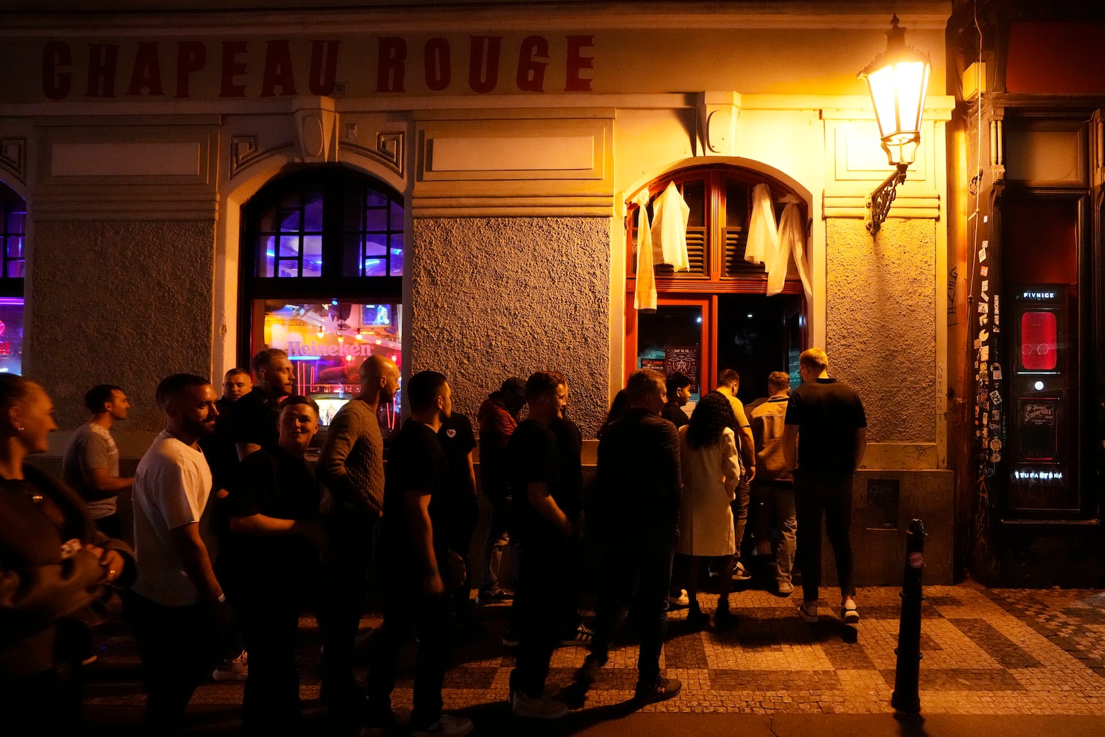 A group of tourists stand in line outside a bar as they attend a pub crawl tour in downtown Prague, Czech Republic, Thursday, Oct. 17, 2024. (AP Photo/Petr David Josek)