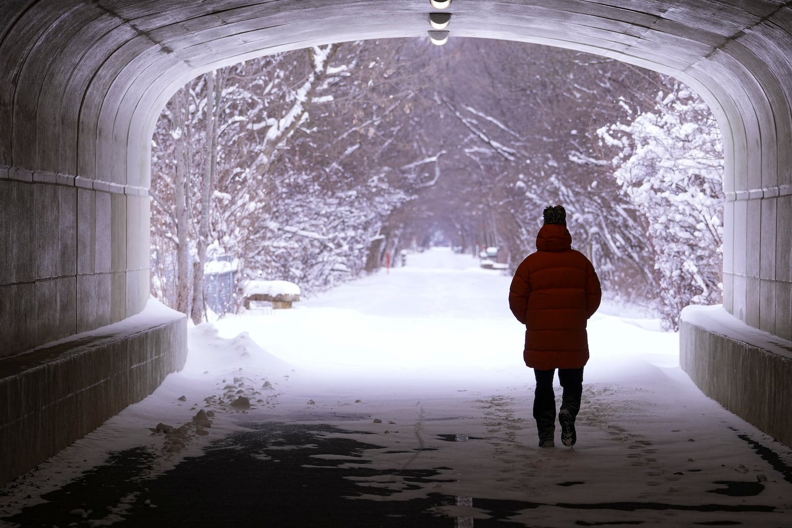 A pedestrian makes their way though a tunnel along the snow-covered Monon Trail in Carmel, Ind., Monday, Jan. 6, 2025. (AP Photo/Michael Conroy)