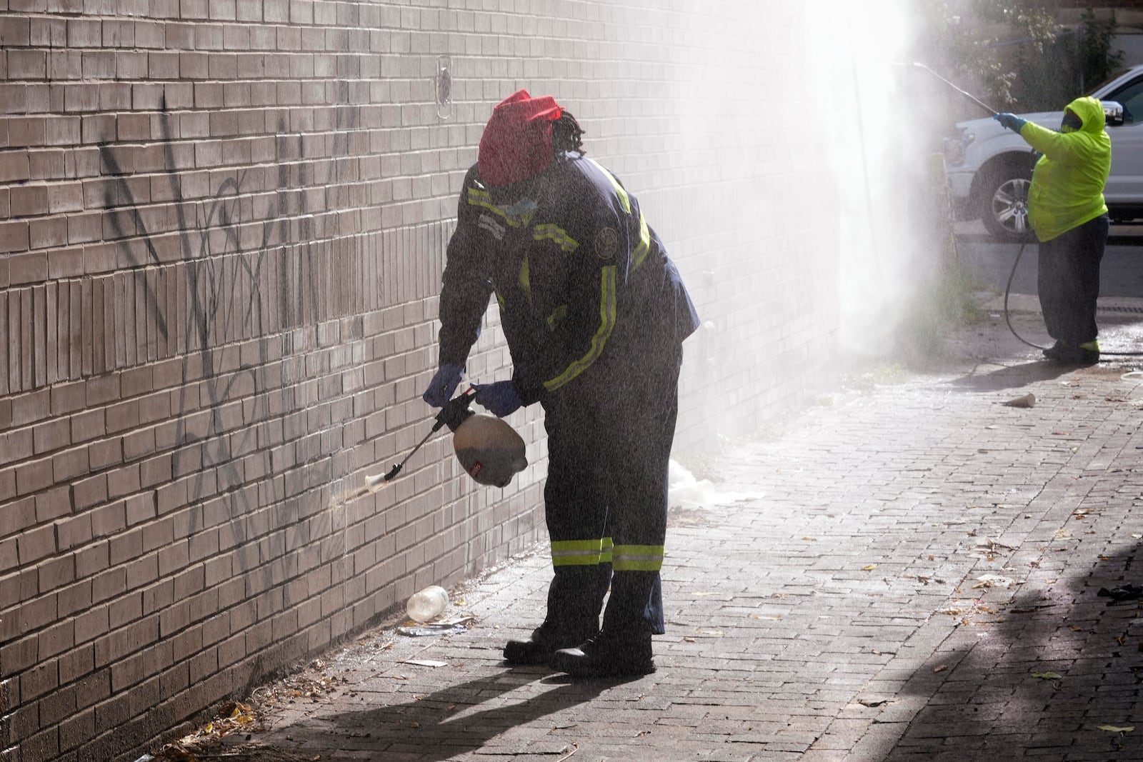 Queen Jones, left, sprays on a chemical to remove graffiti as Dominique Medley, right, uses a pressure washer to remove the graffiti off of a building in Washington, Tuesday, Aug. 20, 2024. (AP Photo/Susan Walsh)