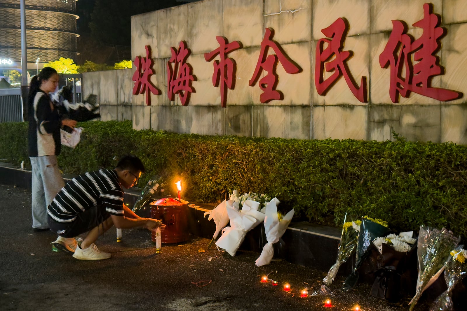 A man lights a candle near flowers placed outside the Zhuhai People's Fitness Plaza, where a man deliberately rammed his car into people exercising at the sports center, killing some and injuring others in Zhuhai in southern China's Guangdong province on Tuesday, Nov. 12, 2024. (AP Photo/Ng Han Guan, File)