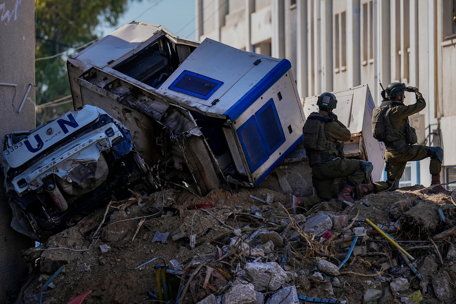 FILE - Israeli soldiers take position next to crumpled-up U.N. vehicles perched precariously atop building debris in UNRWA compound, where the military discovered tunnels in the main headquarters of the U.N. agency that the military says Hamas militants used to attack its forces during a ground operation in Gaza, Thursday, Feb. 8, 2024. (AP Photo/Ariel Schalit, File)