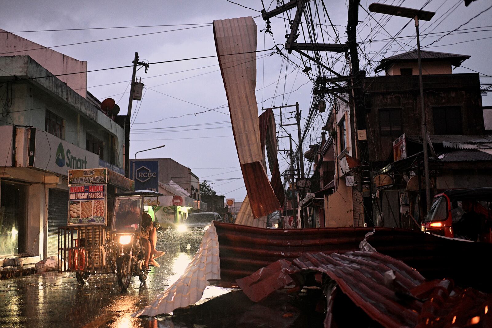 Motorists ride past a part of a roof suspended on electric wires blown by strong winds caused by Typhoon Man-yi along a street in the municipality of Baler, Aurora province, Philippines, Monday, Nov. 18, 2024. (AP Photo/Noel Celis)