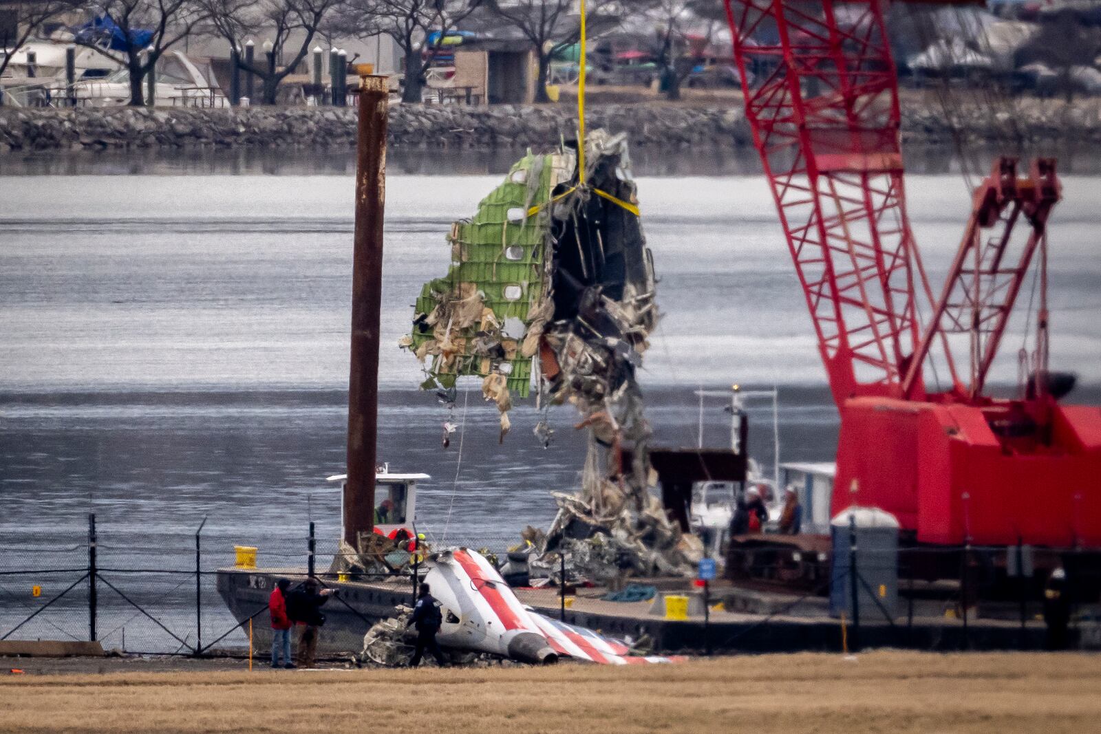 A crane offloads a piece of wreckage from a salvage vessel onto a flatbed truck, near the wreckage site in the Potomac River of a mid-air collision between an American Airlines jet and a Black Hawk helicopter, at Ronald Reagan Washington National Airport, Wednesday, Feb. 5, 2025, in Arlington, Va. (AP Photo/Ben Curtis)