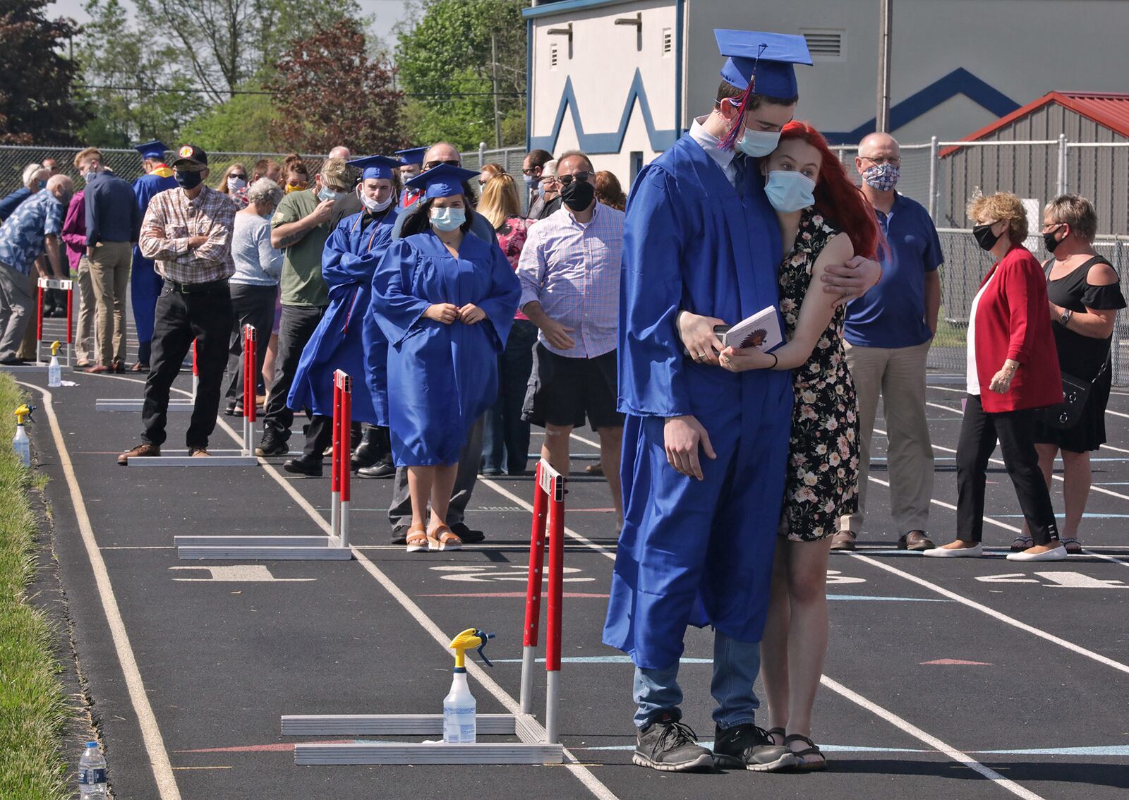 Northwestern senior Michael Akers gets a hug from his girlfriend, Hayley Clark, as he waits with his family to graduate outside at Taylor Field. Students were allowed to bring up to 10 guests and they were staged around the running track in alphabetical order while they waited to receive the diploma. BILL LACKEY/STAFF