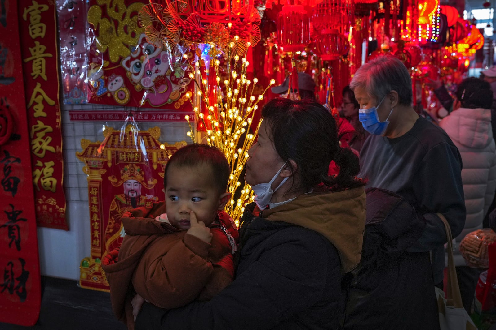 A woman carries a child as she shops at a New Year bazaar set up for the upcoming Chinese Lunar New Year, in Beijing on Jan. 13, 2025. (AP Photo/Andy Wong)