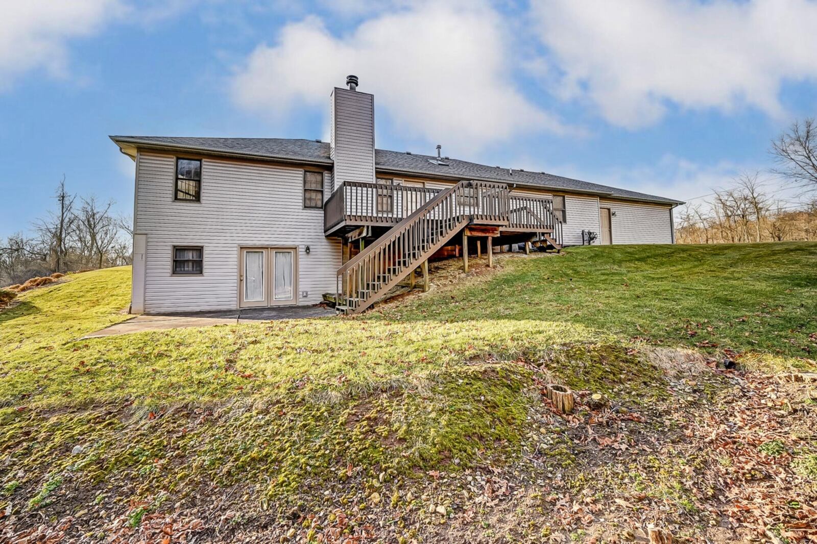 The rear of the home has a wooden deck with railings and steps down to the concrete patio off the walk-out basement