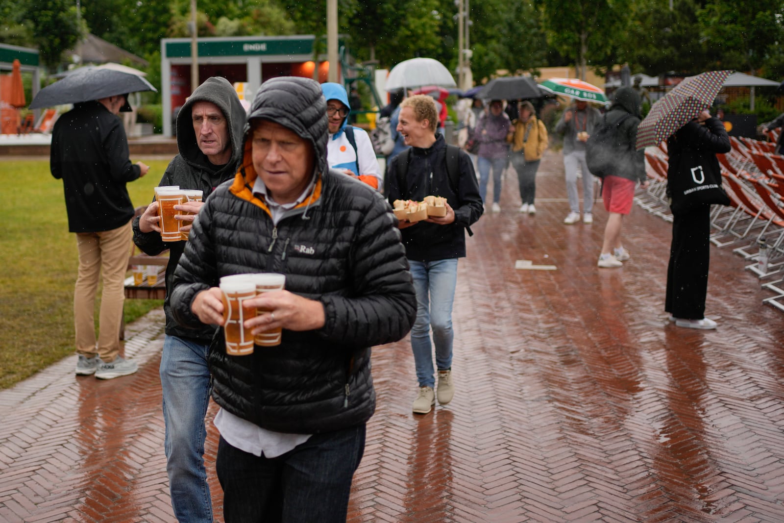 FILE - Tennis fans, some holding beers, shield themselves from the rain during third round matches of the French Open tennis tournament at the Roland Garros stadium in Paris, Friday, May 31, 2024. (AP Photo/Thibault Camus, File)