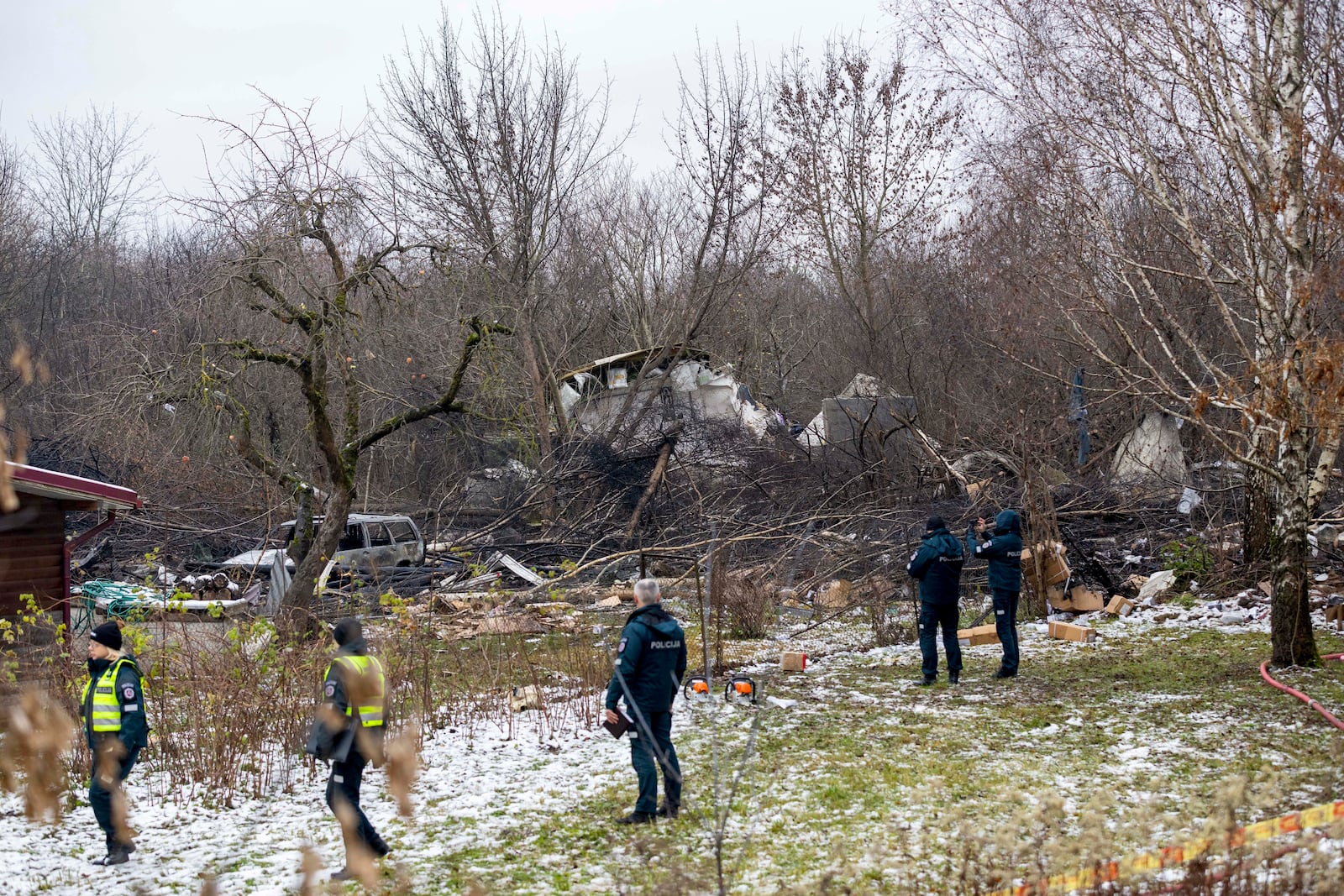 Lithuanian Emergency Ministry employees and police officers stand near the place where a DHL cargo plane crashed into a house near the Lithuanian capital Vilnius, Lithuania, Lithuania, Monday, Nov. 25, 2024. (AP Photo/Mindaugas Kulbis)