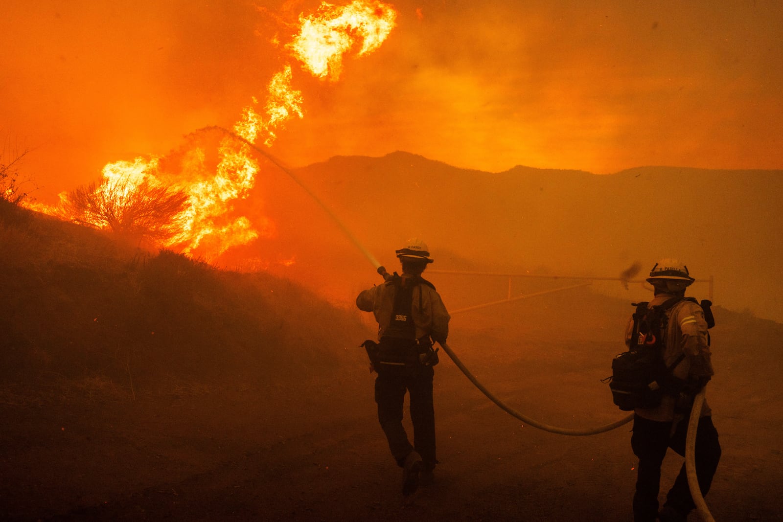 Firefighters spray water as they monitor flames caused by the Hughes Fire along a roadside in Castaic, Calf., Wednesday, Jan. 22, 2025. (AP Photo/Ethan Swope)