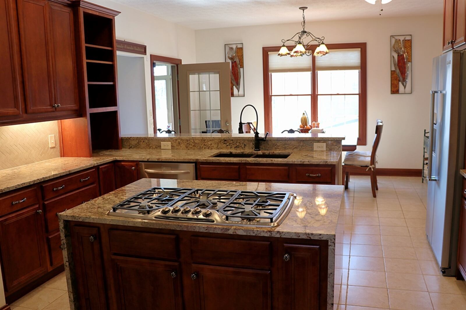 In the kitchen, a dual counter peninsula offers breakfast bar seating and lower-level preparation counter near the hammered-copper dual sink. An island has a five-burner gas cooktop, and there are double-wall ovens. 