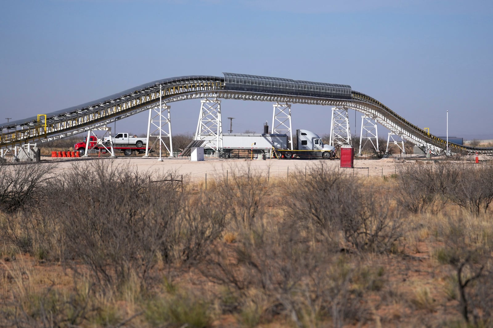 Traffic flows along Route 18 near the Texas/New Mexico state line as a 42-mile conveyor belt by Atlas Energy is seen at a distance carrying sand needed for hydraulic fracturing Wednesday, Feb. 26, 2025, in Kermit, Texas. (AP Photo/Julio Cortez)