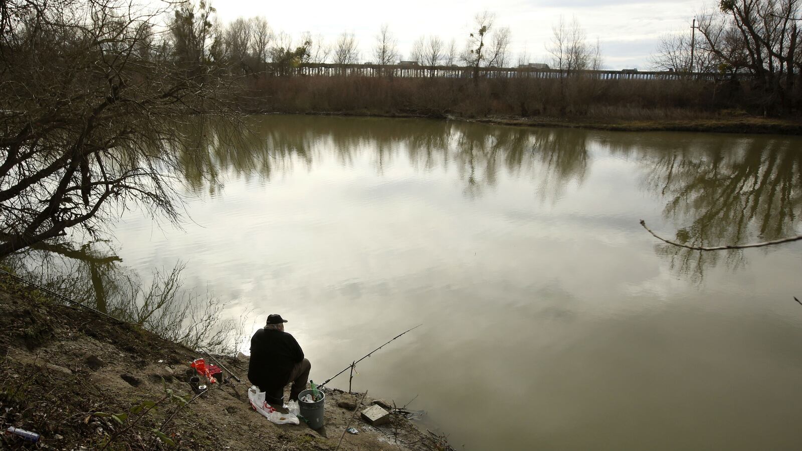 A fisherman sits along the slough Monday Jan. 27, 2020, where the body of an infant, Nikko Lee Perez, was discovered in 2007 near Woodland, Calif. Paul Allen Perez, 57, is accused in the deaths of five of his own infant children over a nine-year span between 1992 and 2001.