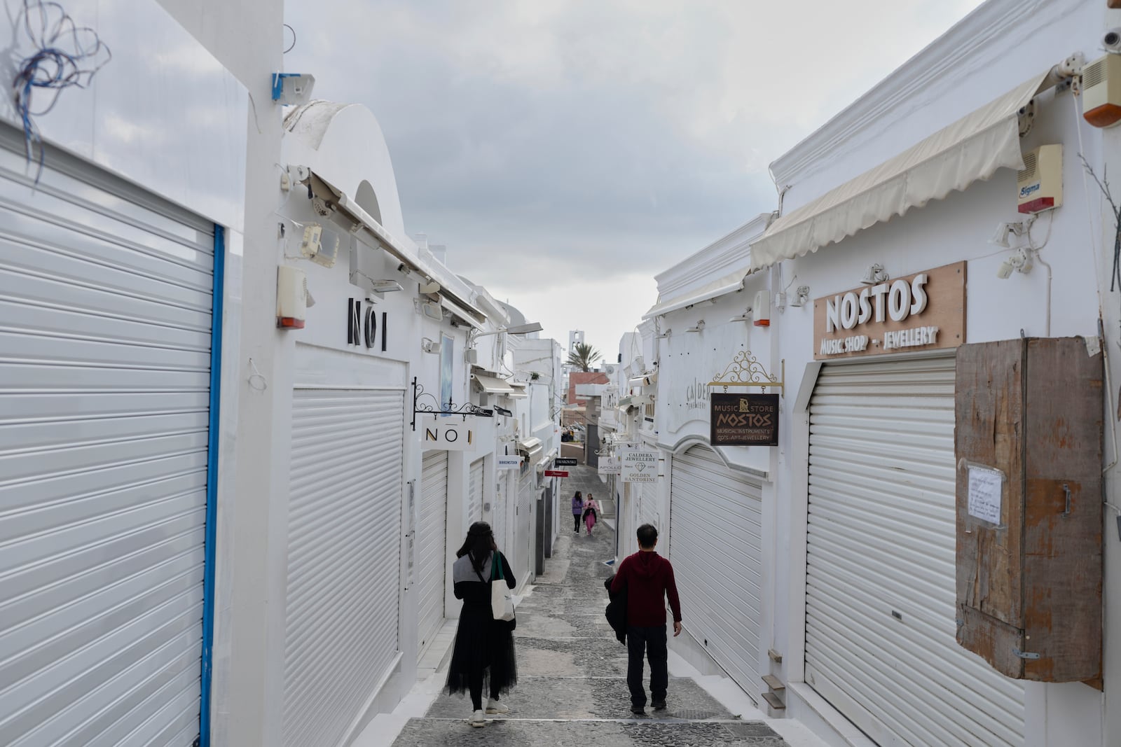 Tourists pass by closed shops in Fira town as Greek authorities are taking emergency measures in response to intense seismic activity on the popular Aegean Sea holiday island of Santorini, southern Greece, Monday, Feb. 3, 2025. (AP Photo/Petros Giannakouris)