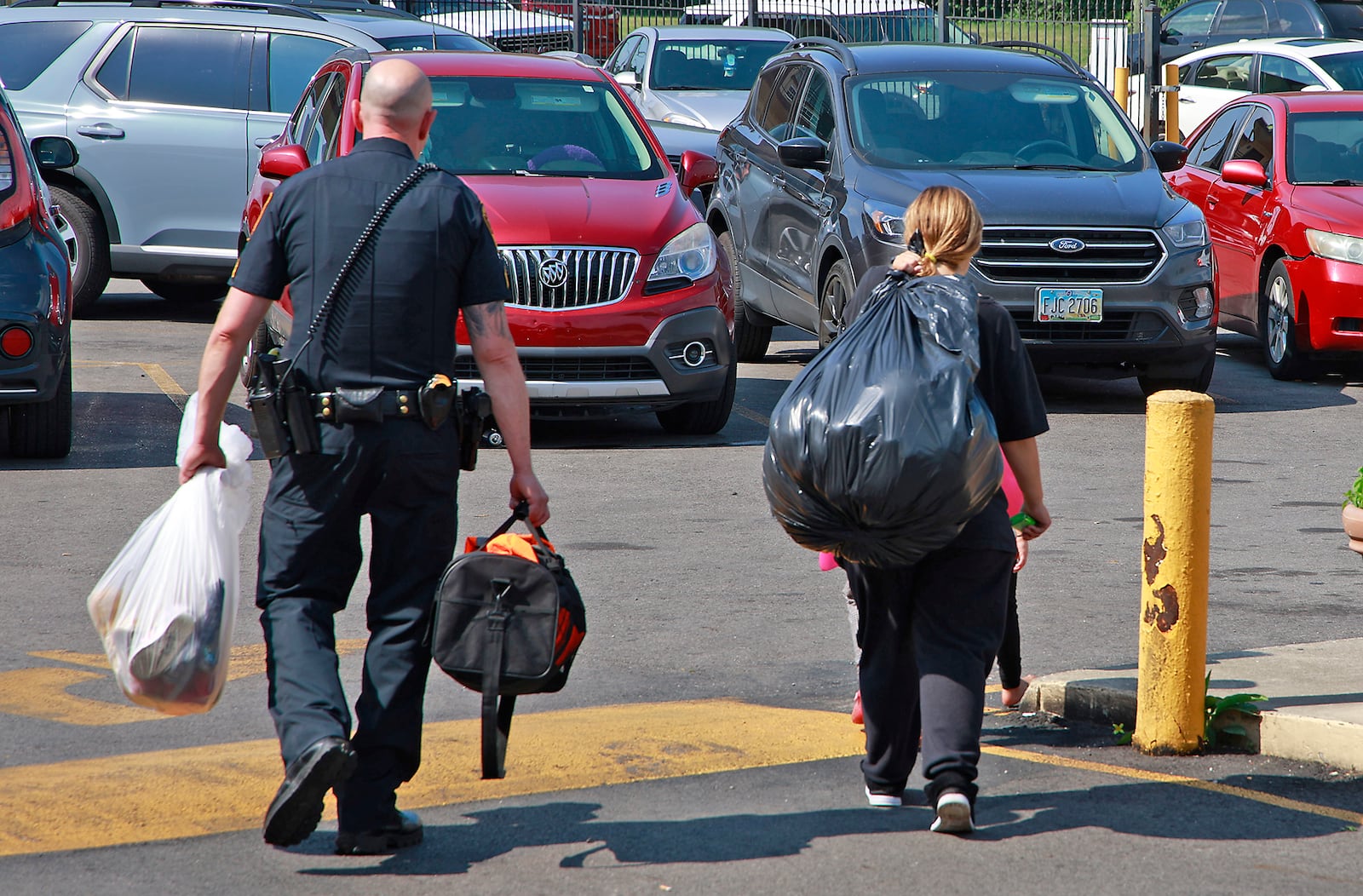 A member of the Springfield Police Division helps a woman carry her family's belongings to their car as they move out of the Executive Inn Tuesday, August 6, 2024. BILL LACKEY/STAFF