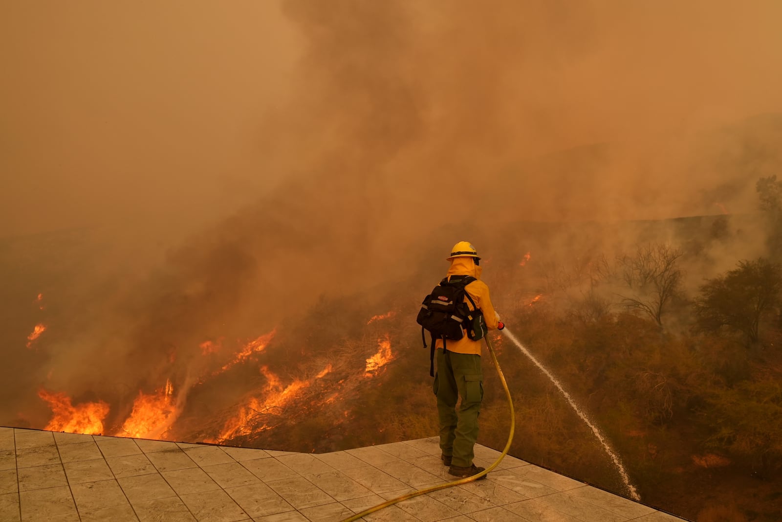 FILE - A firefighter hoses down flames as the Palisades Fire approaches in Mandeville Canyon, Jan. 11, 2025, in Los Angeles. (AP Photo/Jae C. Hong)