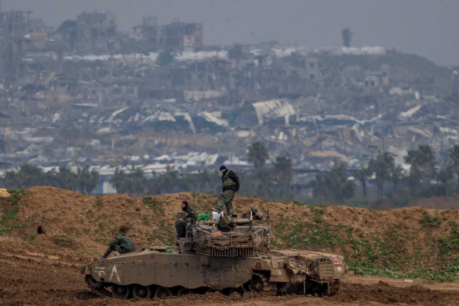 Destroyed buildings by Israeli bombardments inside the northern Gaza Strip can be seen as Israeli soldiers work on their tank in southern Israel, Tuesday, Feb.11, 2025. (AP Photo/Ariel Schalit)