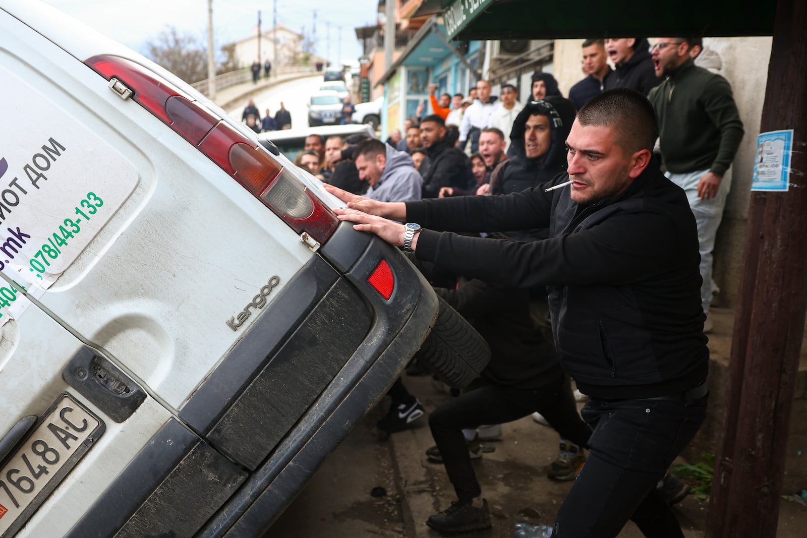 People push a car on its side while protesting near the home of the owner of a nightclub that was the scene of a massive fire, after a vigil for the victims in the town of Kocani, North Macedonia, Monday, March 17, 2025. (AP Photo/Armin Durgut)