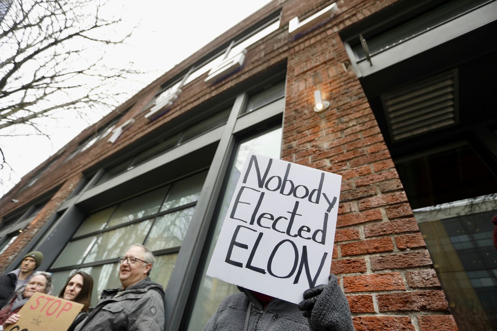 A person protesting Elon Musk's actions in the Trump administration holds a sign outside a Tesla showroom in Seattle on Thursday, Feb. 13, 2025. (AP Photo/Manuel Valdes)