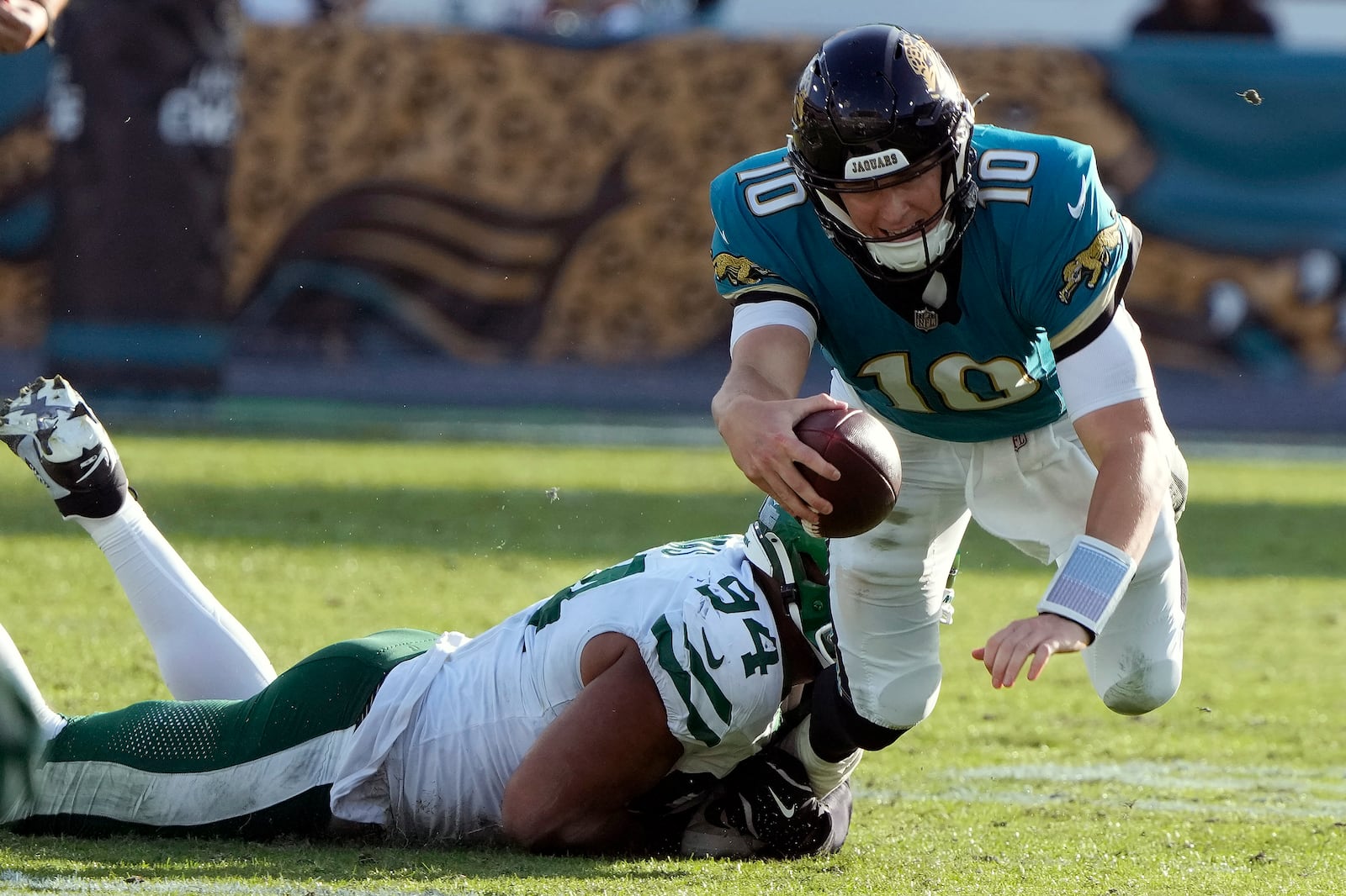 Jacksonville Jaguars quarterback Mac Jones (10) is tripped up by New York Jets defensive end Solomon Thomas (94) during the second half of an NFL football game Sunday, Dec. 15, 2024, in Jacksonville, Fla. (AP Photo/John Raoux)