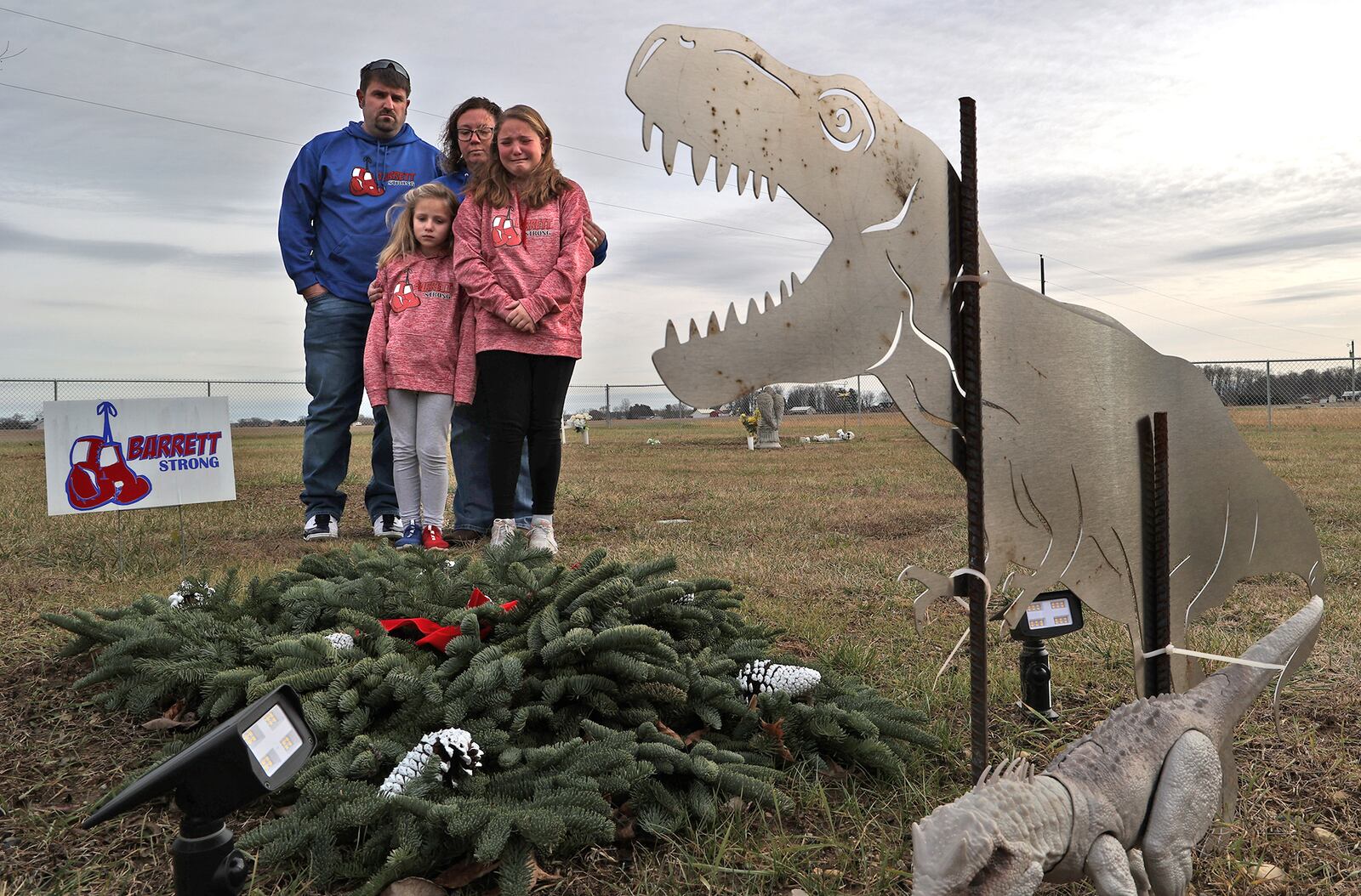 Barrett Fitzsimmons' parents Brad and Lana along with his sisters  Brayden and Braelynn look over Barrett's grave at Myers Cemetery in Pike Township. Two years after Barrett died at the age of 9-years-old from cancer the family is still not permitted to place a permanent headstone on his grave because of a disagreement with the cemetery trustees over the design.  A metal cutout of a dinosaur, which Barrett loved, is the only thing that marks the grave. BILL LACKEY/STAFF