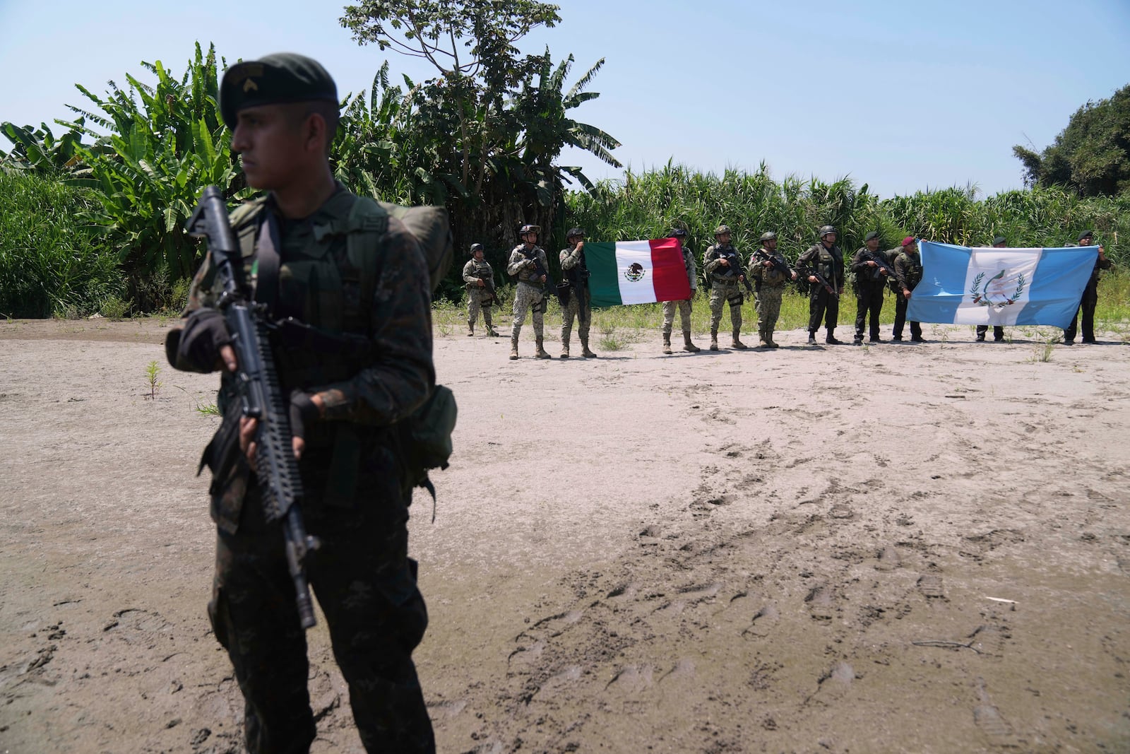 Guatemalan soldiers, right, hold up a national flag alongside Mexican soldiers, at the shared border as part of Guatemala's Ring of Fire operation, aiming to strengthen border control, at the Suchiate River in Ocos, Guatemala, Thursday, March 13, 2025. (AP Photo/Moises Castillo)