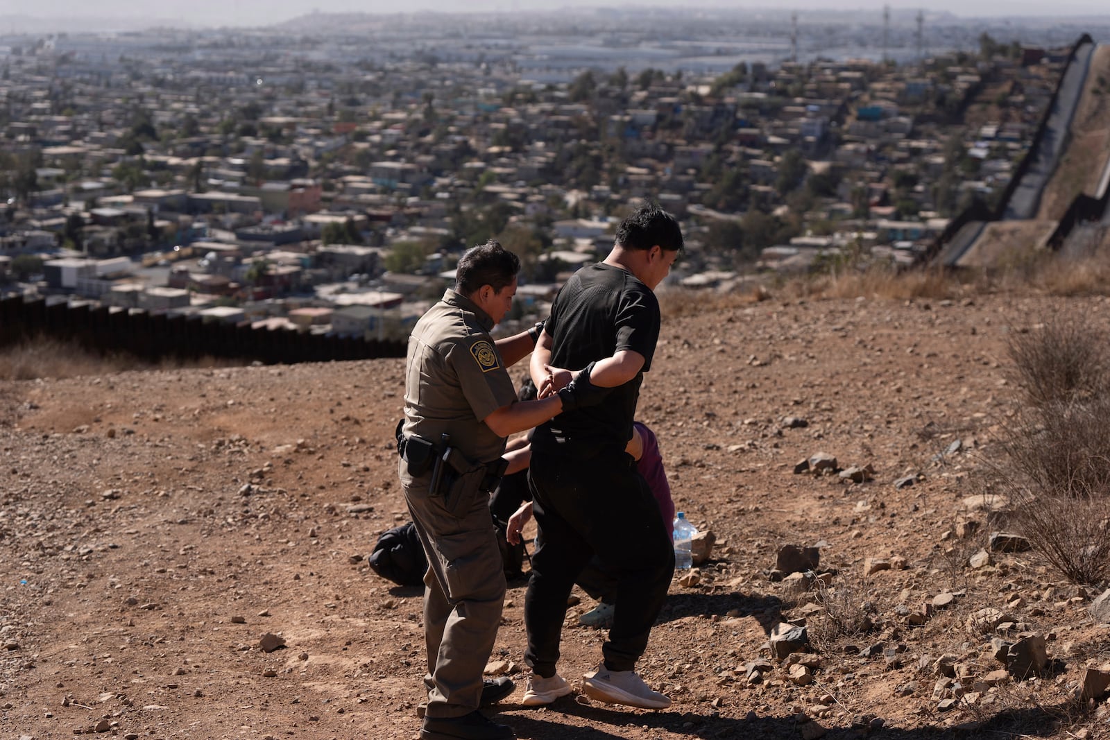 Border Patrol Agent Gutierrez, left, escorts one of four men after the group crossed the border illegally through a gap in two walls separating Mexico from the United States before turning themselves in, Thursday, Jan. 23, 2025, in San Diego. (AP Photo/Gregory Bull)