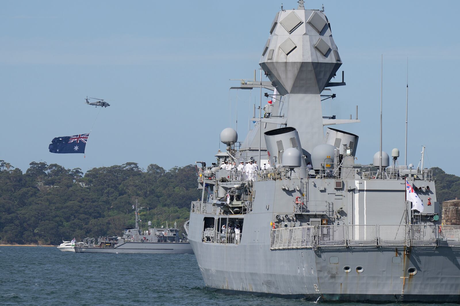 A helicopter flies with a giant Australian flag over the harbor ahead of Britain's King Charles III arrival at the Sydney Opera House in Sydney, Australia, Tuesday, Oct. 22, 2024. (AP Photo/Mark Baker, Pool)