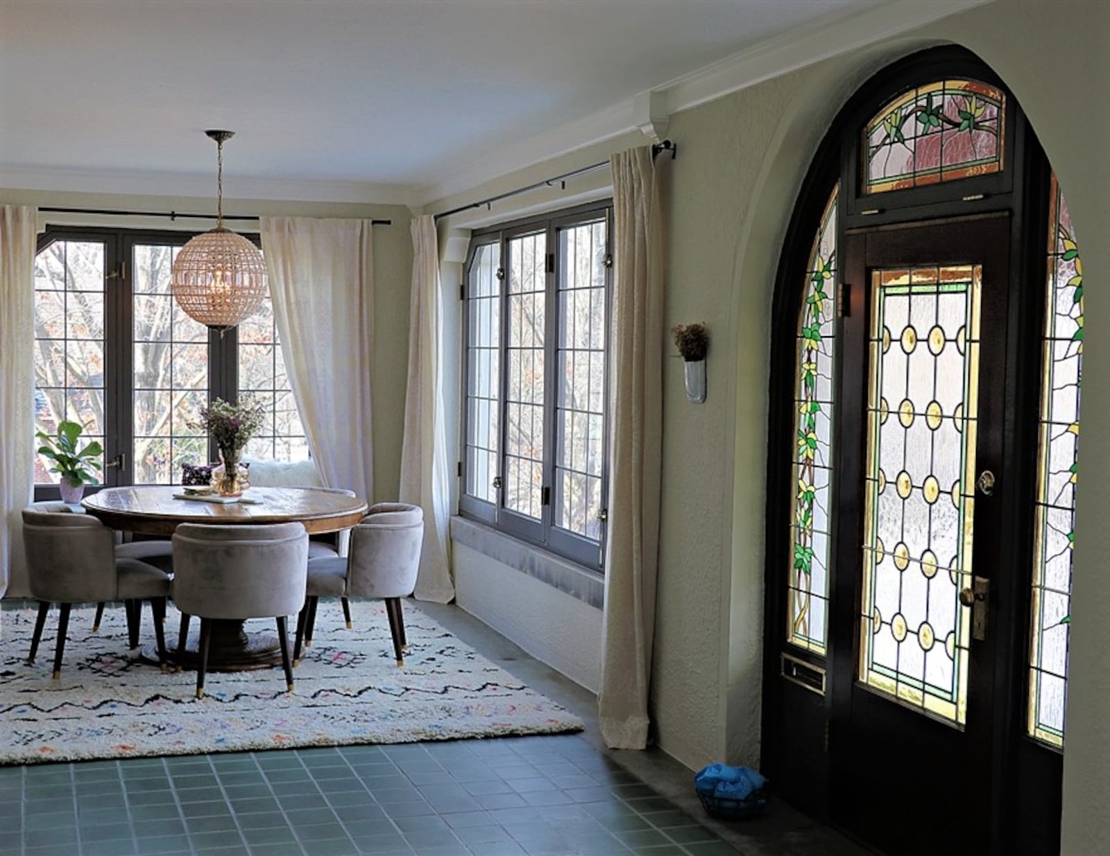 Tiffany-stained glass within the arched door frame provides a clue to the details within. The doors open into a four-season room with large windows and repolished turquoise ceramic-tile flooring. 