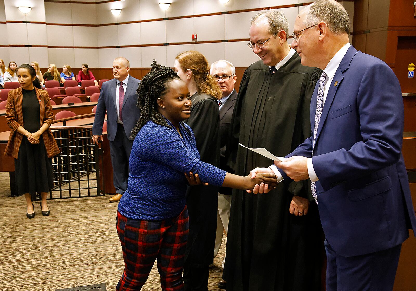 Jennifer Muhawe, a native of Uganda who now lives in Dayton, receives her certificate of citizenship from U.S. District Court Judge Michael J. Newman and University of Dayton President Dr. Eric F. Spina during a naturalization ceremony Monday, Sept. 18, 2023. BILL LACKEY/STAFF