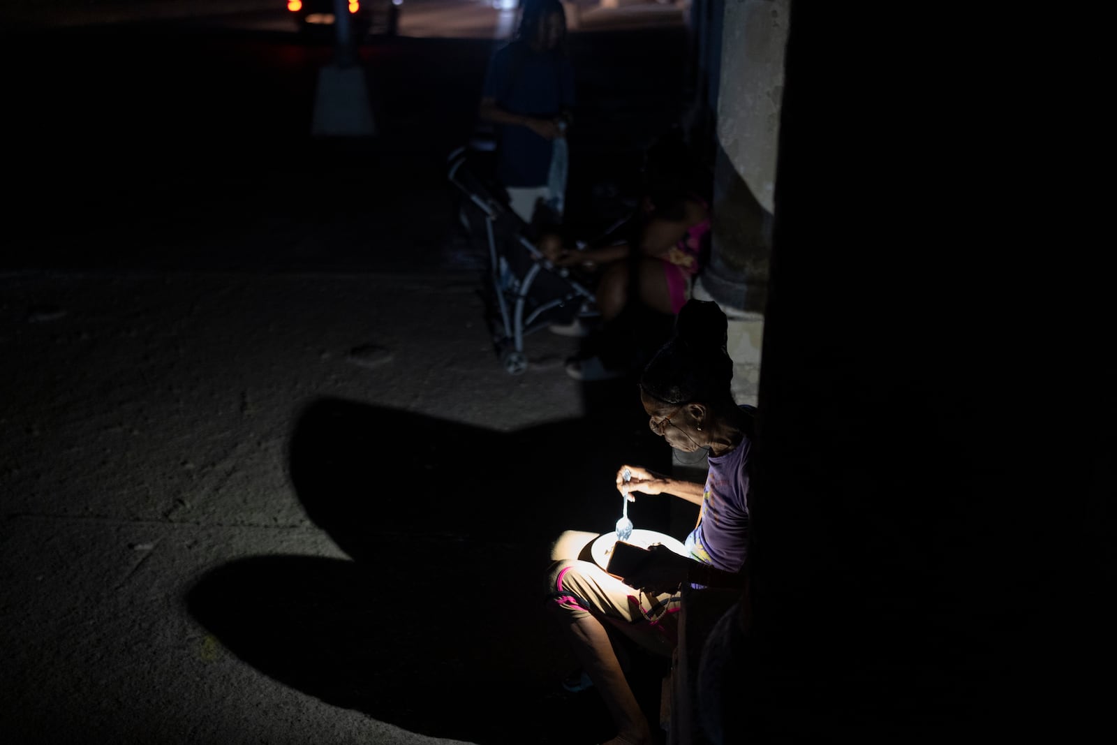 A woman illuminates her plate of food with her phone's flashlight on a street during a general blackout in Havana, Cuba, Friday, March 14, 2025. (AP Photo/Ramon Espinosa)