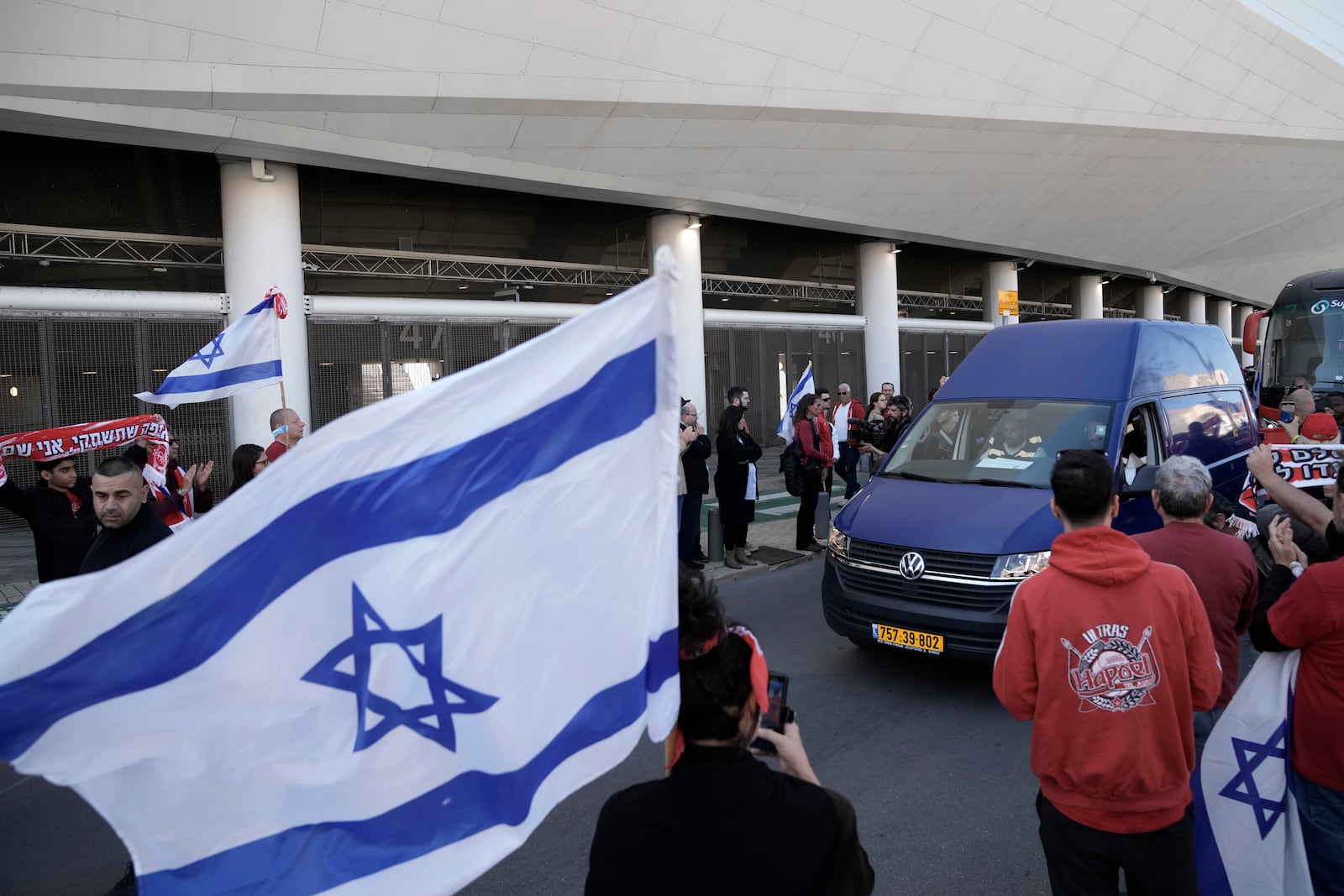 Friends, family and soccer fans at a public memorial ceremony for slain hostage Tsachi Idan, a fan of Hapoel Tel Aviv F.C., who was killed in Hamas captivity in the Gaza Strip, watch a van carrying his coffin outside of Bloomfield Stadium in Tel Aviv, Israel, Friday, Feb. 28, 2025. (AP Photo/Leo Correa)