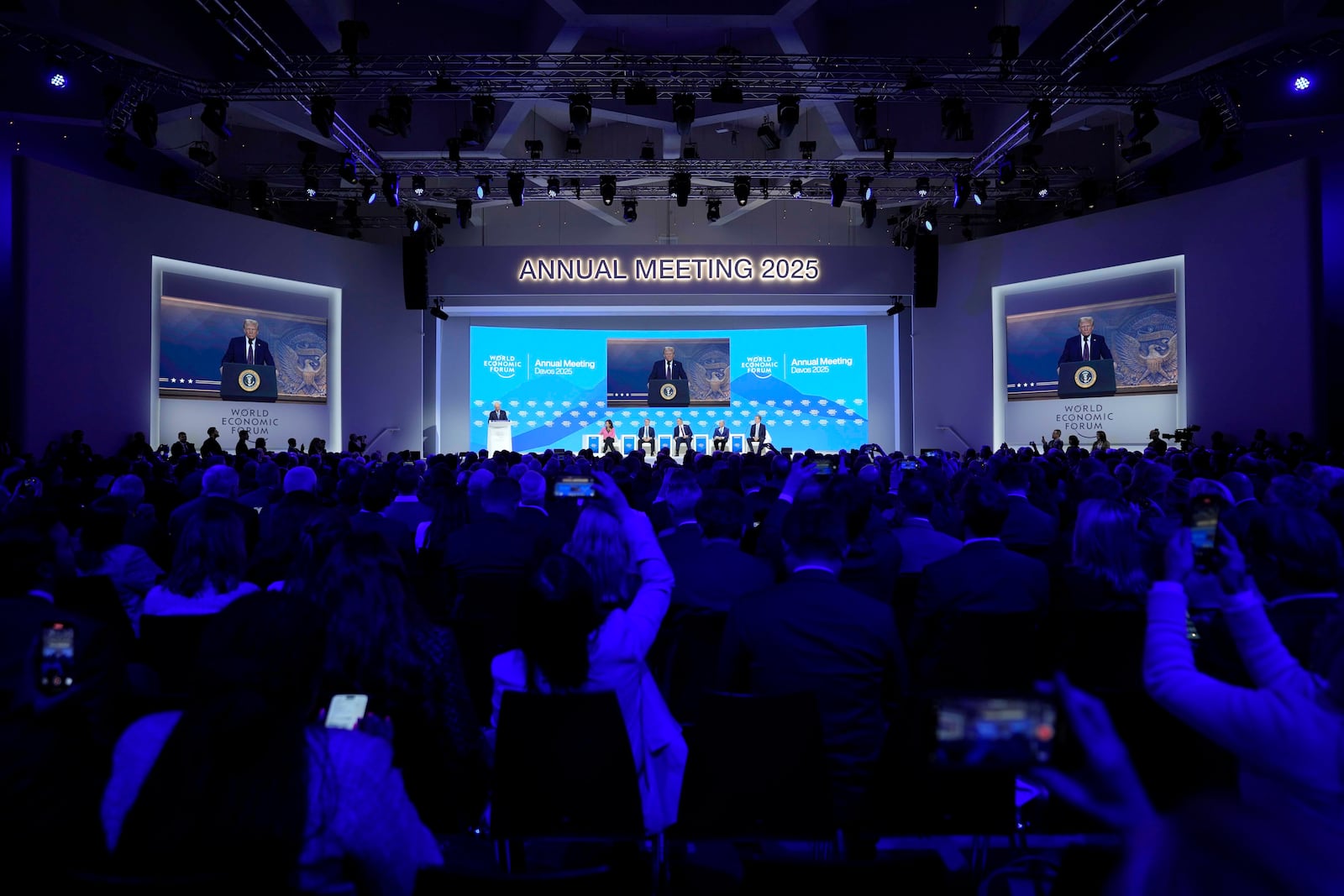 People follow a virtual speech of U.S. president Donald Trump at the Annual Meeting of World Economic Forum in Davos, Switzerland, Thursday, Jan. 23, 2025. (AP Photo/Markus Schreiber)