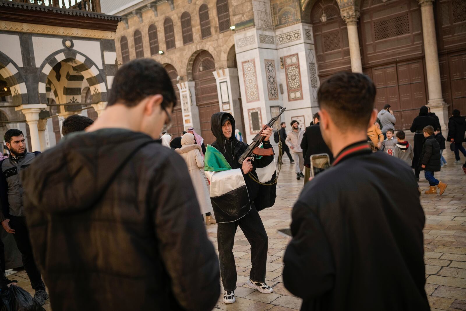 A young man poses holding a gun before Friday prayer at the Umayyad mosque in Damascus, Syria, Friday, Dec. 12, 2024. (AP Photo/Leo Correa)