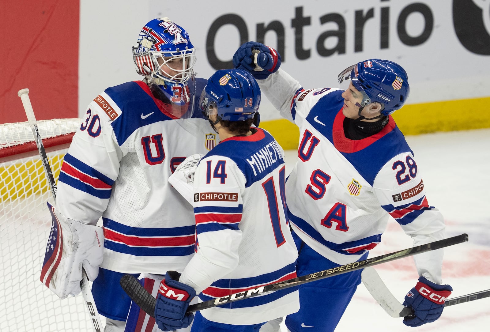 United States defenseman Aram Minnetian (14) and defenseman Zeev Buium (28) congratulate goaltender Hampton Slukynsky after a IIHF World Junior Hockey Championship tournament game against Latvia, Saturday, Dec.28, 2024 in Ottawa, Ontario. (Adrian Wyld/The Canadian Press via AP)