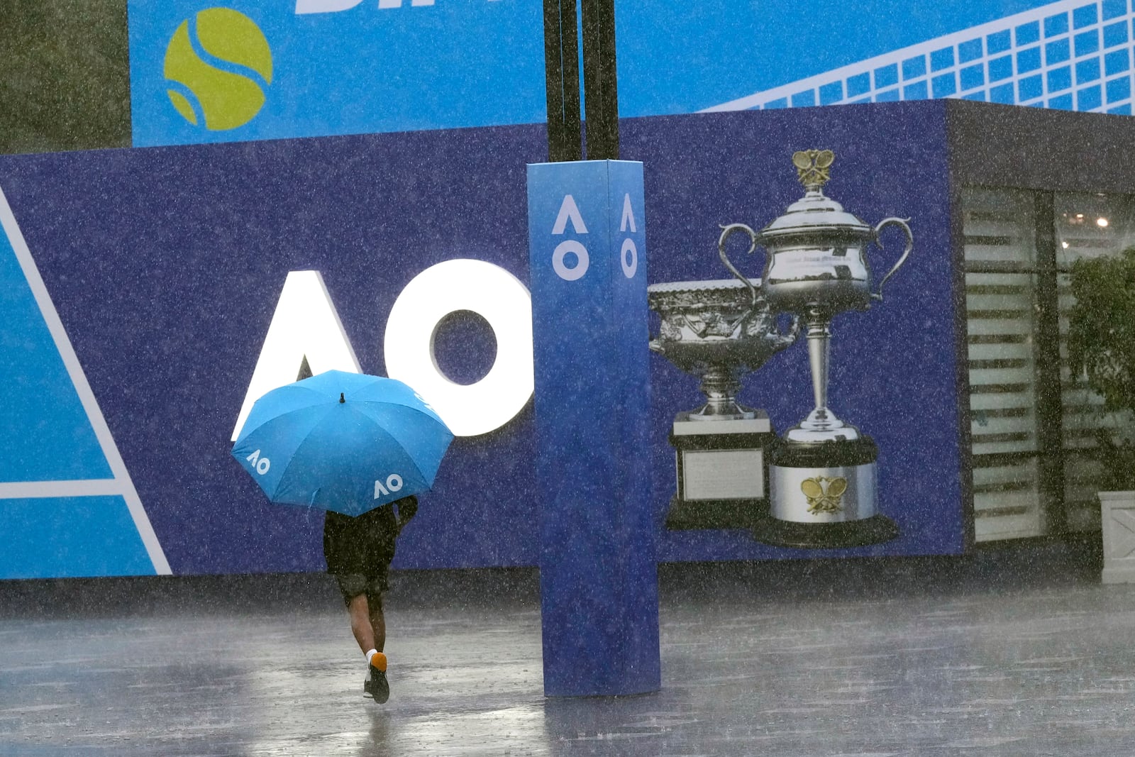 A spectator runs as play is suspended for rain during first round matches at the Australian Open tennis championship in Melbourne, Australia, Sunday, Jan. 12, 2025. (AP Photo/Manish Swarup)